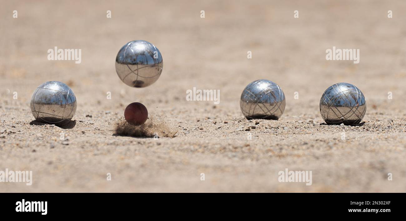 Petanque Ball Boules Schalen auf einem Staubboden, Foto beim Aufprall. Bälle und ein kleiner Holzheber Stockfoto