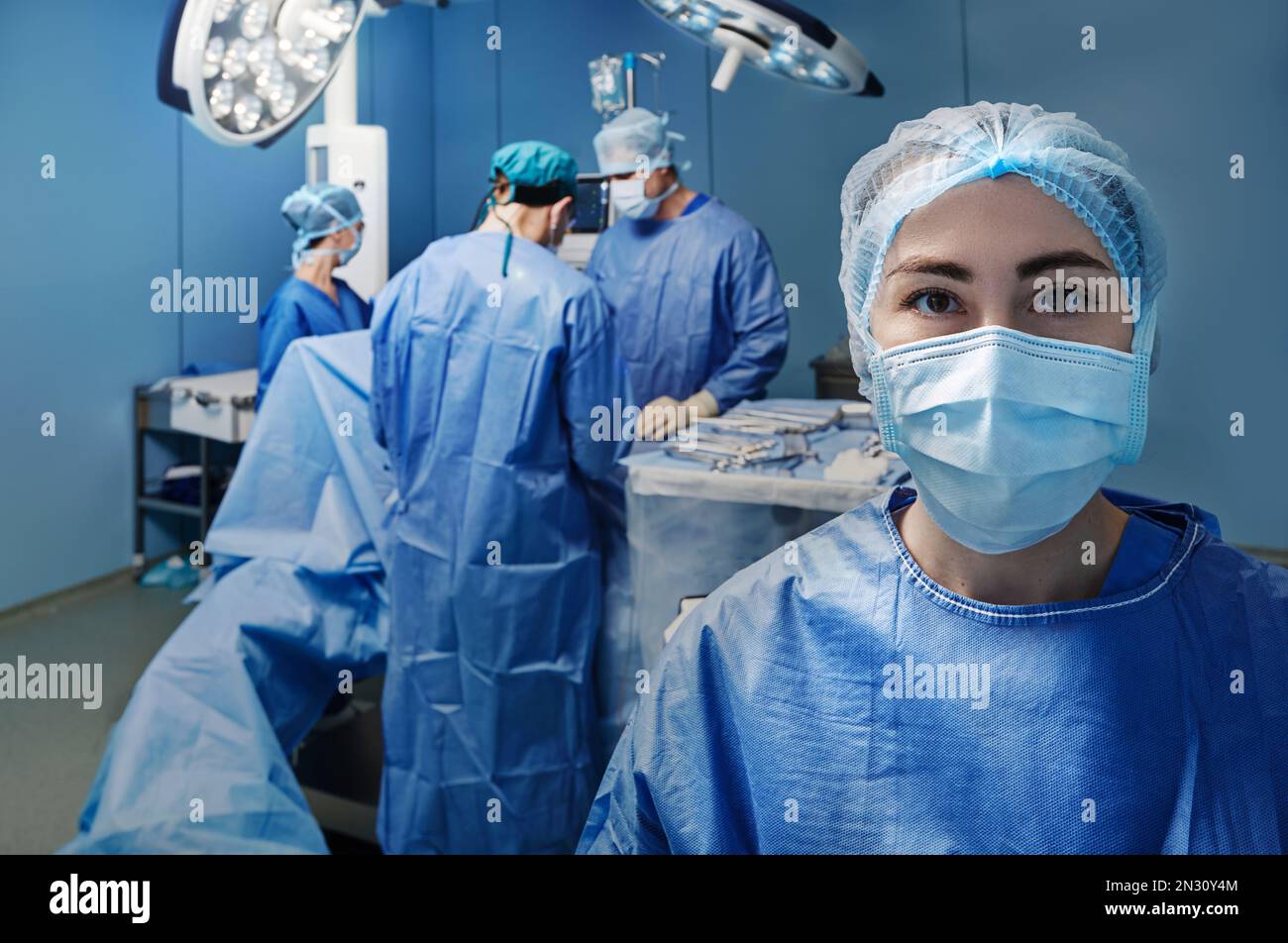 Operationskrankenschwester. Portrait der chirurgischen Krankenschwester trägt medizinische Peeling und Gesichtsschutzmaske über Hintergrund Operationsraum mit Operationspersonal Stockfoto