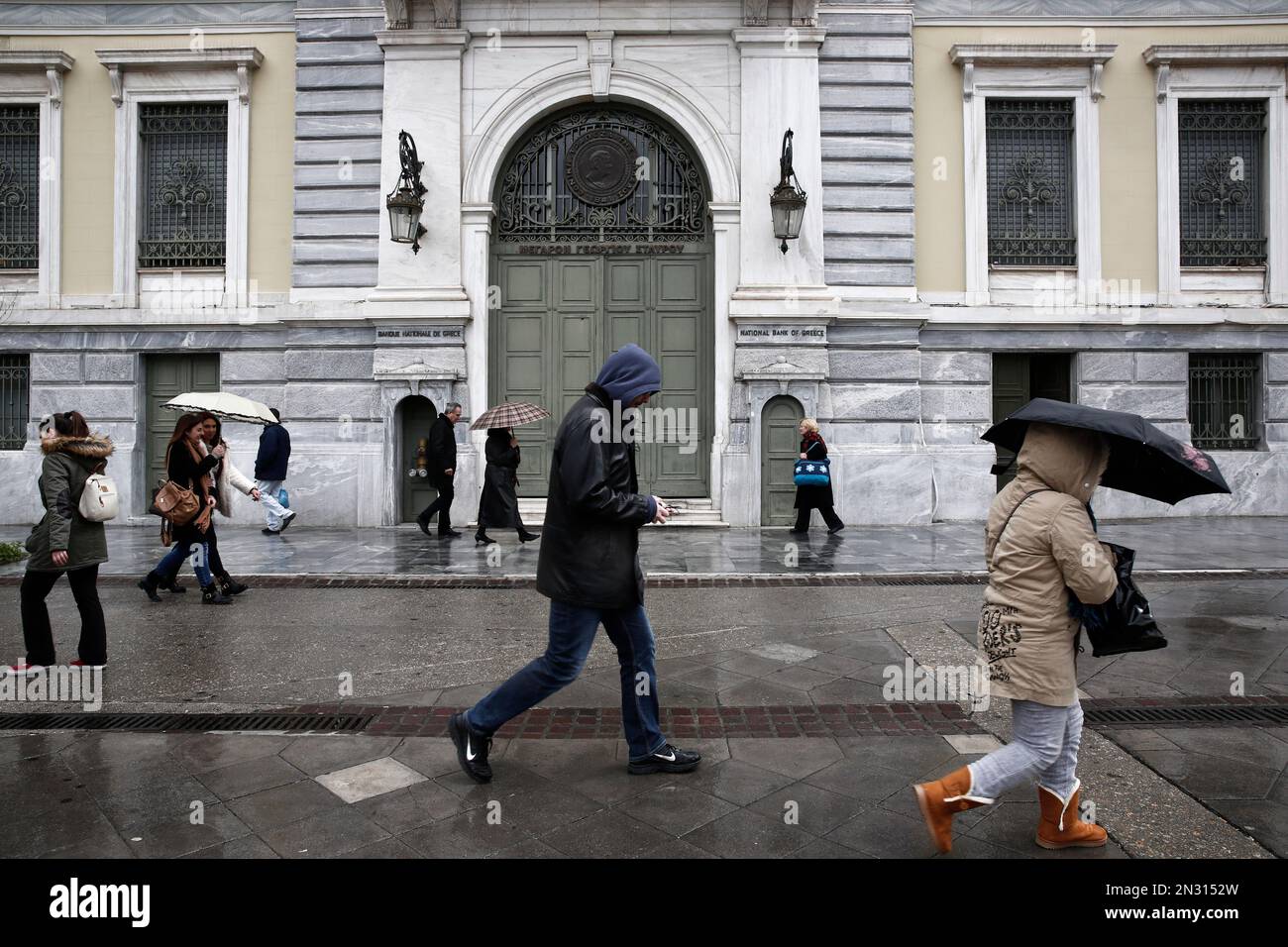 People walk outside the headquarters of the National Bank of Greece, in Athens, Saturday, Feb. 14, 2015. This week, the European Central Bank gave the green light for Greek banks to use another five billion Euro from the Emergency Liquidity Assistance mechanism in order to compensate for continuing deposit withdrawals. (AP Photo/Petros Giannakouris) Stockfoto