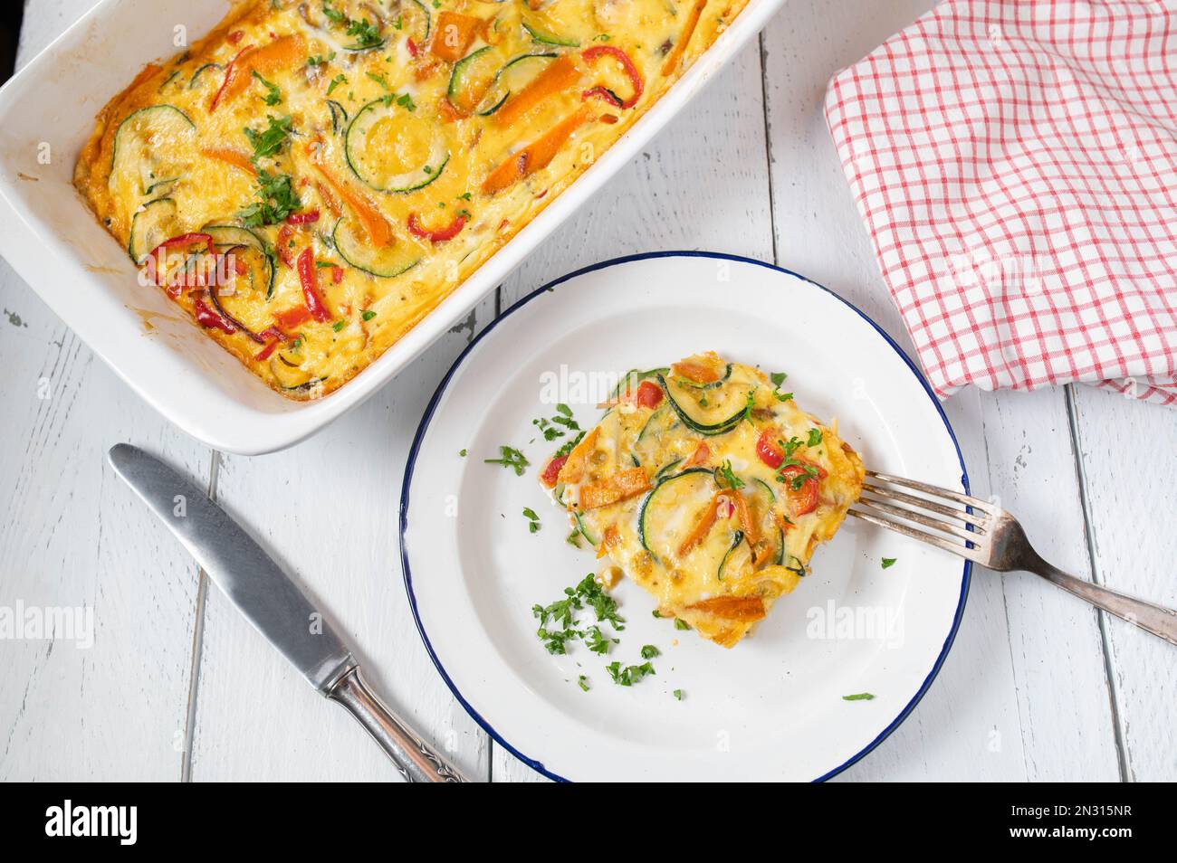 Frittata mit mediterranem Gemüse wie Tomaten, Karotten, Zucchini, Zwiebeln, Paprika und Kräutern in einer Backform auf weißem Hintergrund. Stockfoto