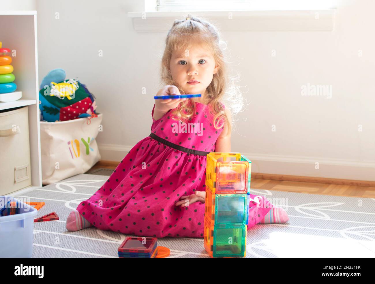 Kleines Kind, das mit Magnetfliesen spielt. Ein kleines, kaukasisches Mädchen spielt. Stockfoto