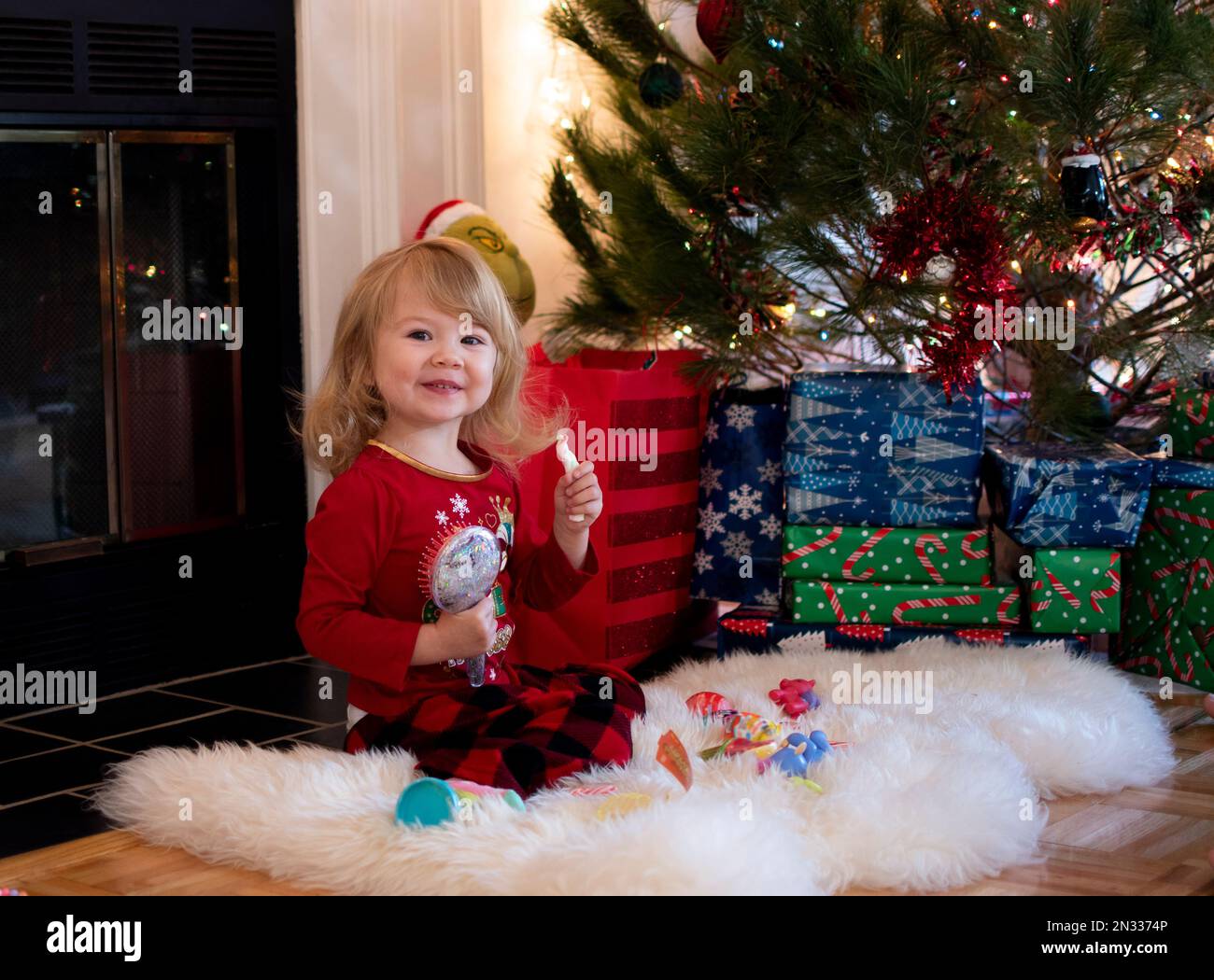 Glückliches süßes blondes kaukasisches Kleinkind unter dem Weihnachtsbaum an einem Weihnachtsmorgen. Eröffnungsgeschenke für Kinder Stockfoto