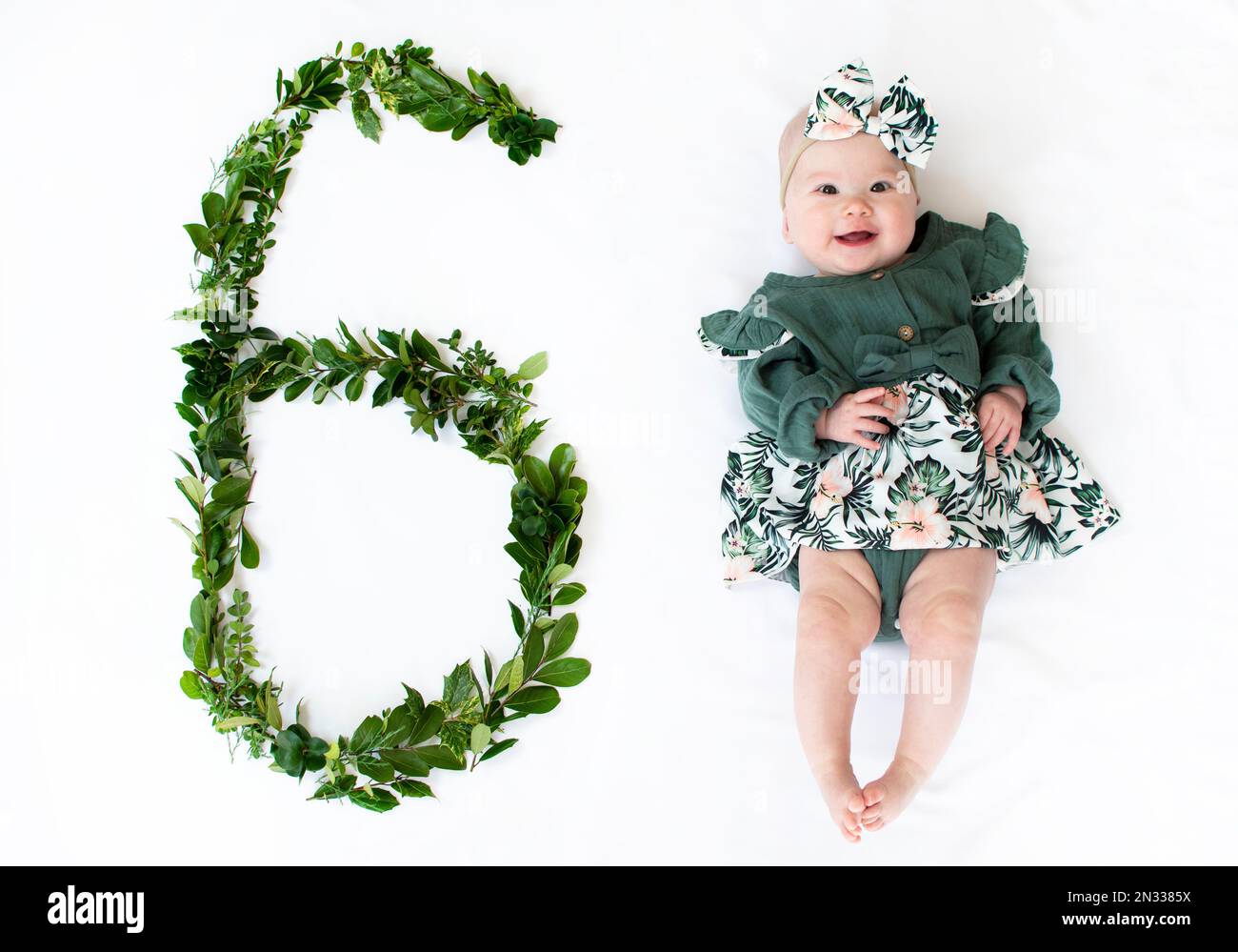 6 Monate altes Mädchen in einem grünen Kleid. Baby-Meilenstein sechs Monate. Stockfoto