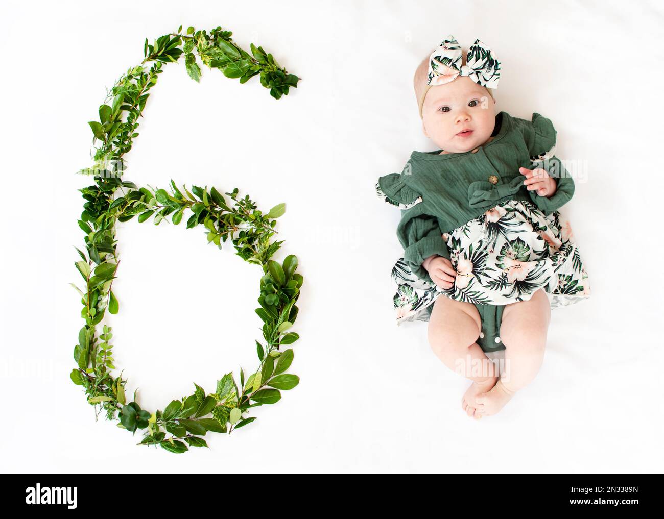 6 Monate altes Mädchen in einem grünen Kleid. Baby-Meilenstein sechs Monate. Stockfoto