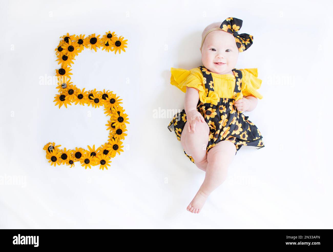 5 Monate altes Mädchen in einem Kleid mit den Blumen. Baby-Meilenstein fünf Monate. Stockfoto