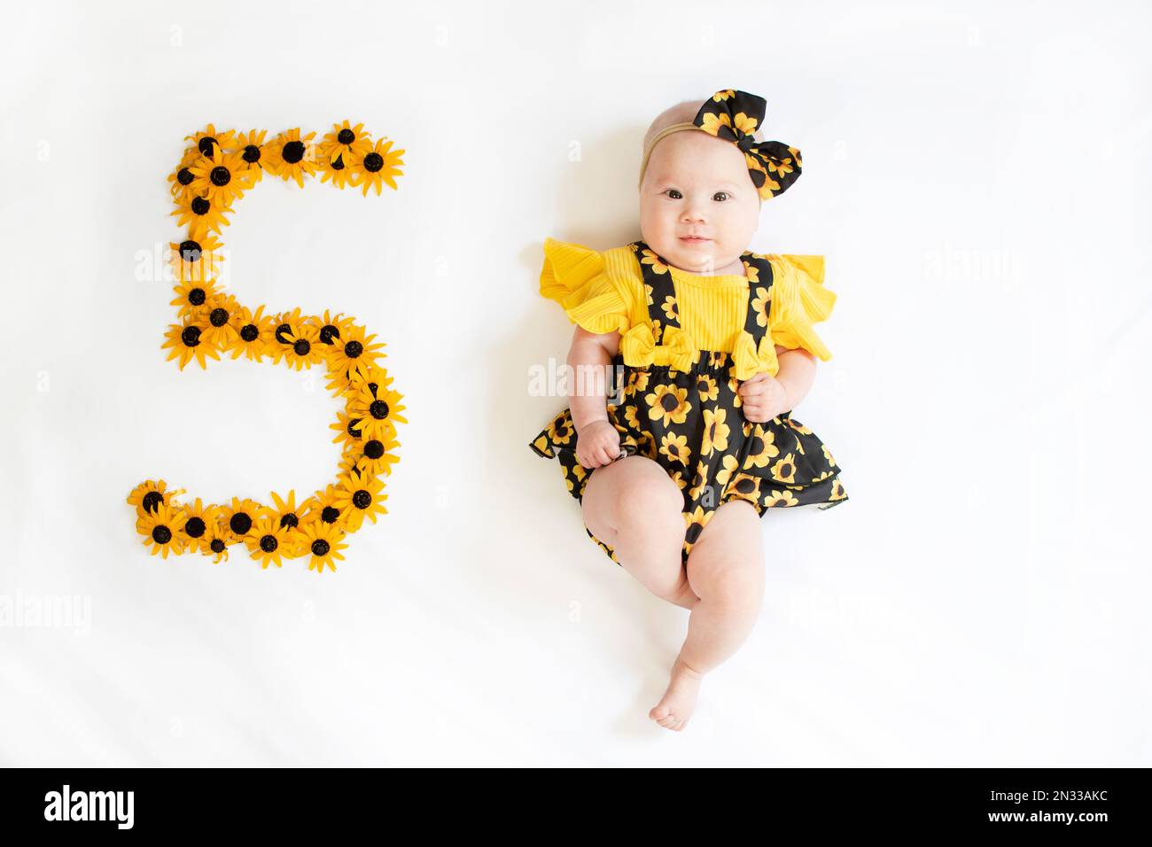 5 Monate altes Mädchen in einem Kleid mit den Blumen. Baby-Meilenstein fünf Monate. Stockfoto