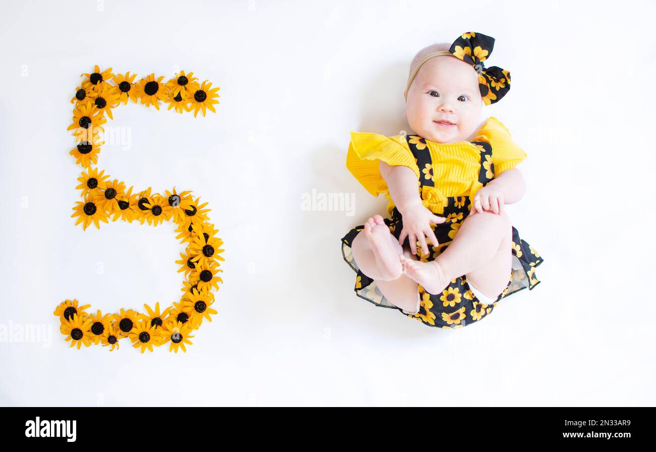 5 Monate altes Mädchen in einem Kleid mit den Blumen. Baby-Meilenstein fünf Monate. Stockfoto