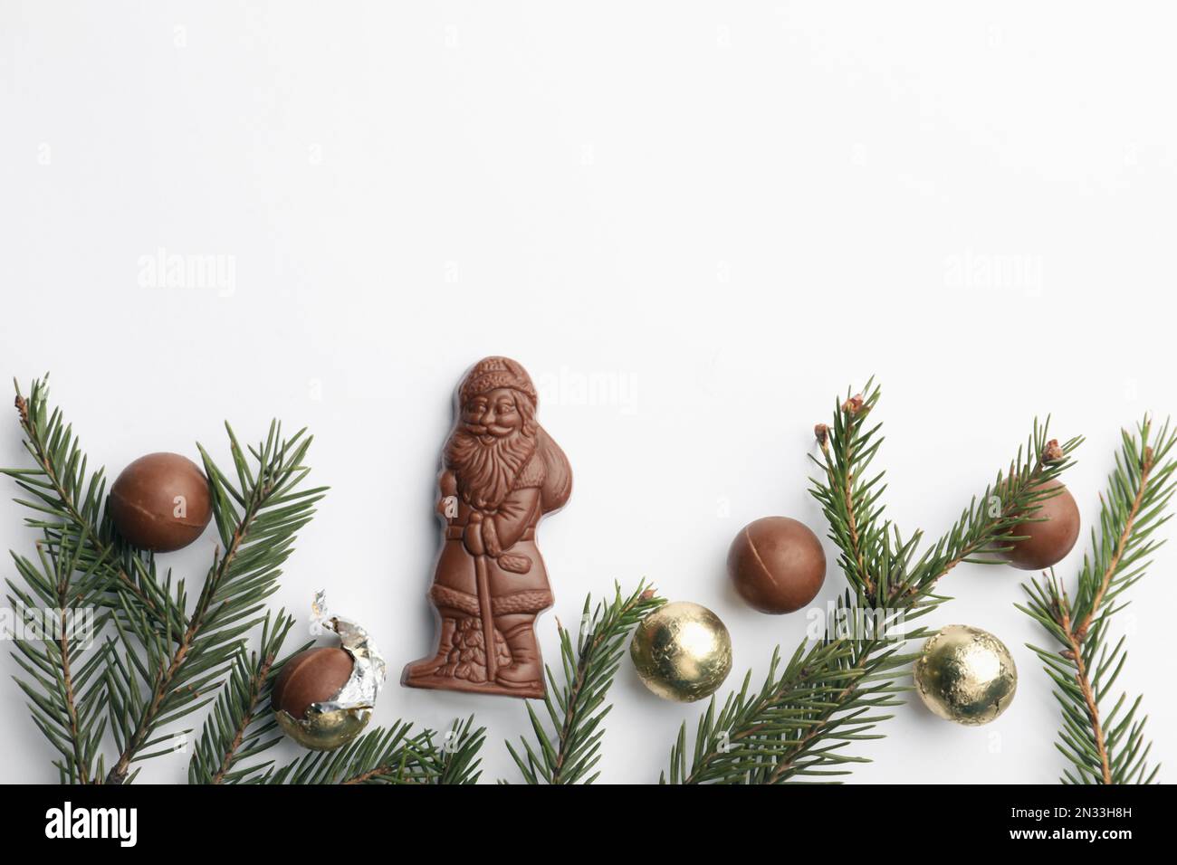 Flache Laienzusammensetzung mit Schokoladenweihnachtsmann, Tannenzweigen und Süßigkeiten auf weißem Hintergrund, Platz für Text Stockfoto