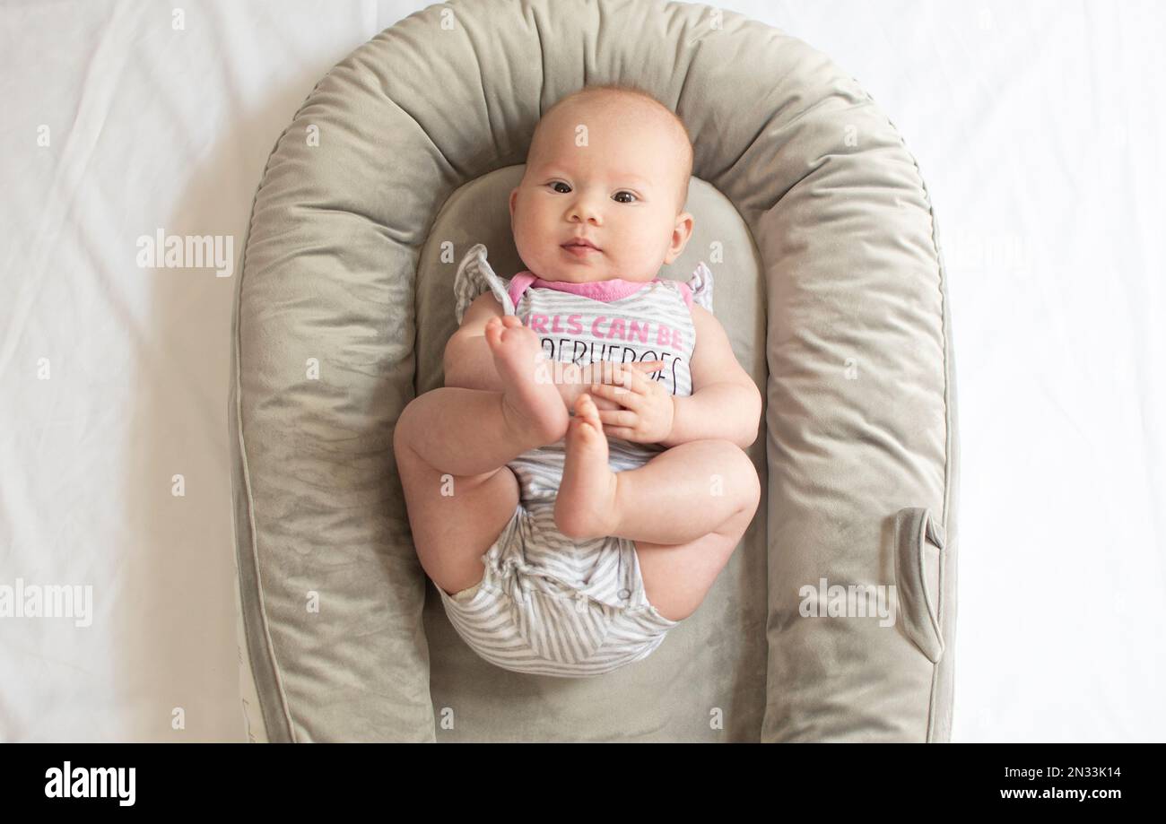 Süßes weißliches neugeborenes Mädchen im Babynest, das mit den Füßen spielt. Baby-Meilensteine Stockfoto