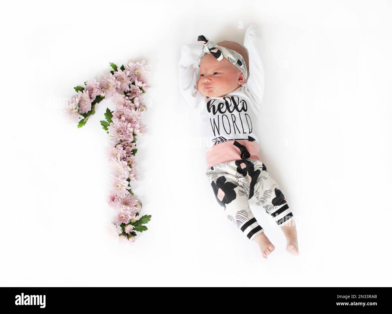 1 Monate altes Mädchen mit rosa Blumen. Ein Baby-Meilenstein für einen Monat. Ein Monat altes Neugeborenes. Kindergeburtstage Stockfoto