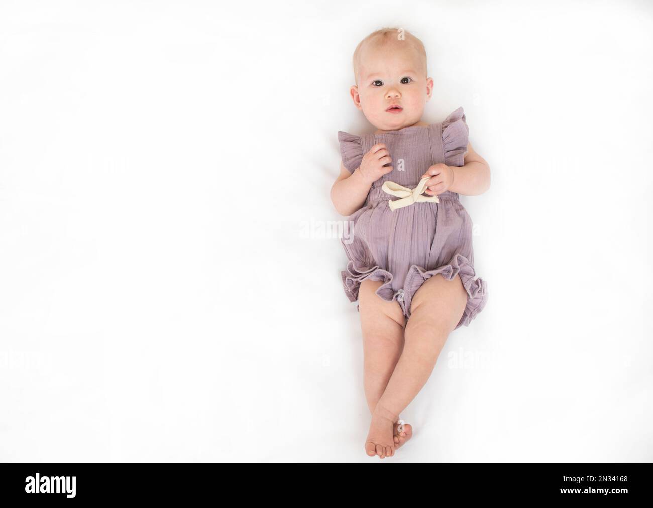 Kaukasisches Baby auf weißem Hintergrund. 9 Monate altes Mädchen in einem Strampler. Stockfoto