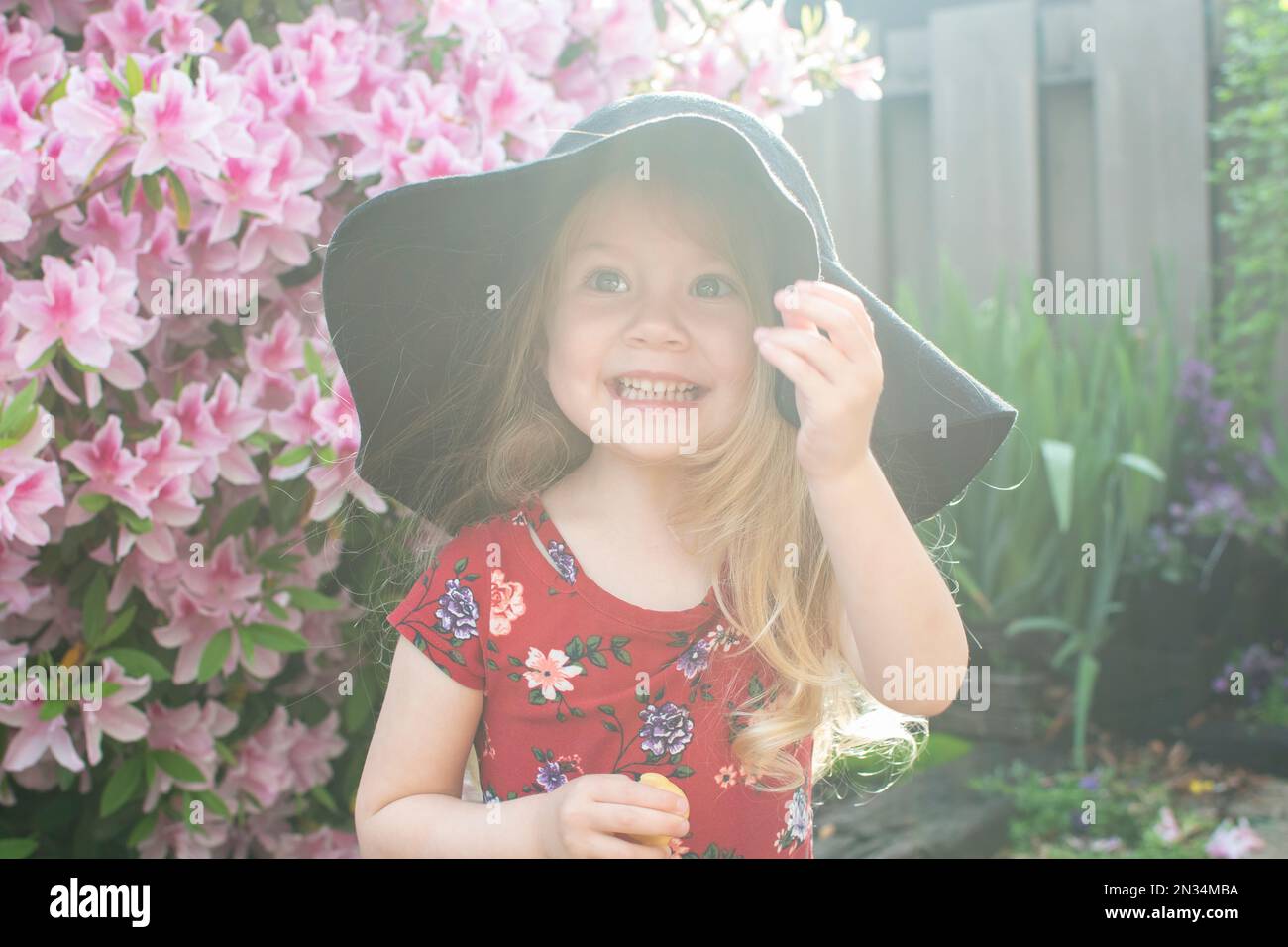 Lächelndes, süßes, weißhäutiges, blondes Kleinkind mit Hut, das den Sommer und den sonnigen Tag draußen genießt Stockfoto