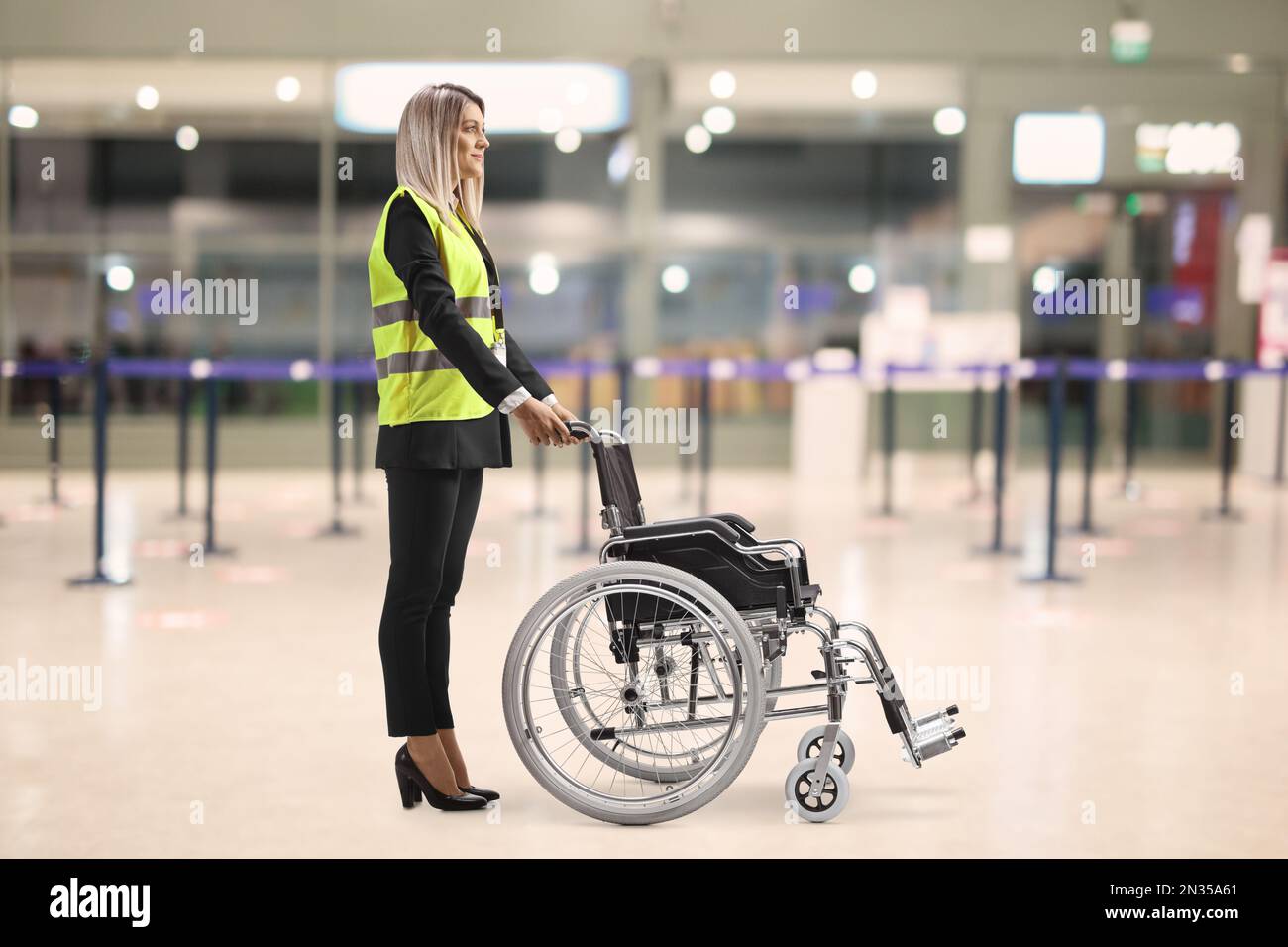 Weibliche Hilfskraft am Flughafen, die mit einem leeren Rollstuhl steht Stockfoto