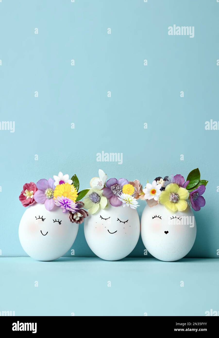 Lustige Ostereier, handgezeichnete Gesichter. Osterferienkonzept mit süßen handgemachten Eiern in Blumenkranzkronen Stockfoto