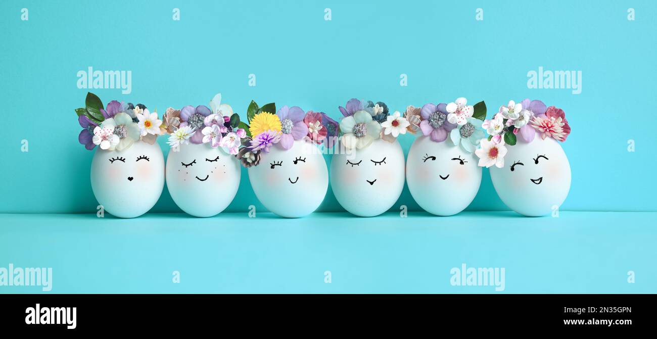 Lustige Ostereier, handgezeichnete Gesichter. Osterferienkonzept mit süßen handgemachten Eiern in Blumenkranzkronen Stockfoto