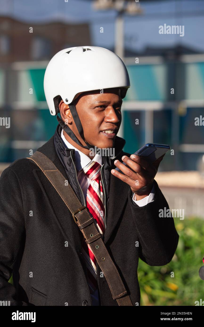 Durchgehende vertikale Aufnahme eines farbigen, gutaussehenden Mannes auf einem Elektromotorradfahrer in ihren 30s, gekleidet mit einem Elektromotorrad und einer Laptop-Tasche bei Stockfoto