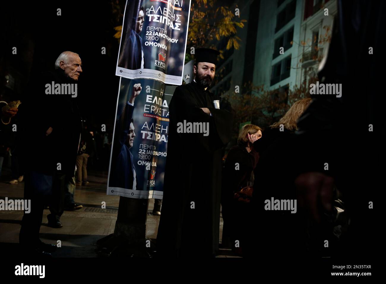 A Greek Orthodox priest stands next to a poster of Alexis Tsipras, leader of Greece's Syriza left-wing main opposition party, before his pre-election speech at Omonia Square in Athens, Thursday, Jan. 22, 2015. Prime Minister Antonis Samaras' New Democracy party has failed so far to overcome a gap in opinion polls with the anti-bailout Syriza party ahead of the Jan. 25 general election. (AP Photo/Petros Giannakouris) Stockfoto