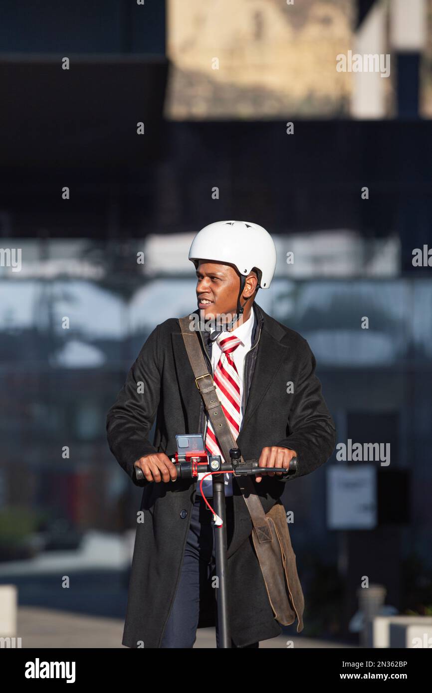Junger Geschäftsmann im Anzug, der auf einem elektrischen Roller bei einem Geschäftstreffen fährt. Umweltfreundliches Verkehrskonzept Stockfoto