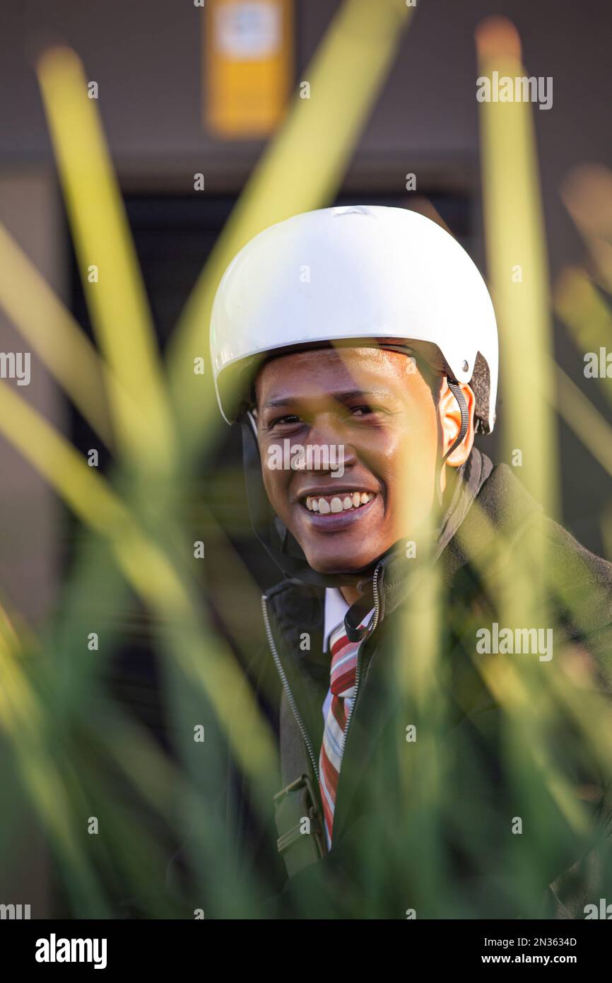 Lateinamerikanischer Geschäftsmann mit einem lächelnden Fahrradhelm, der in die Kamera schaut. Stockfoto