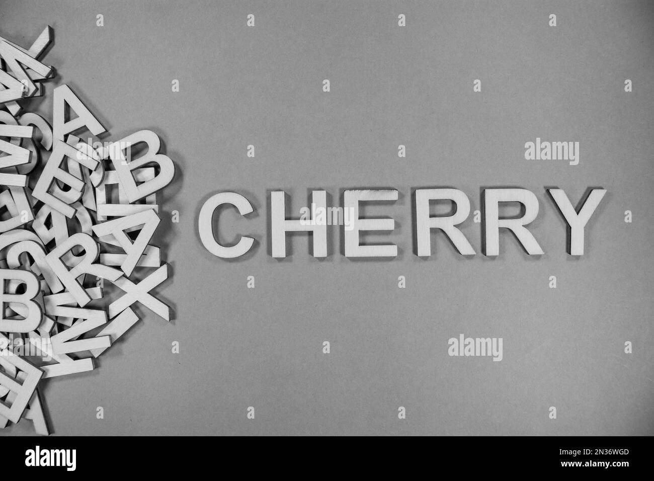KIRSCHE in englischsprachigen Großbuchstaben, die aus einem Stapel schwarz-weißer Buchstaben herausfließen Stockfoto