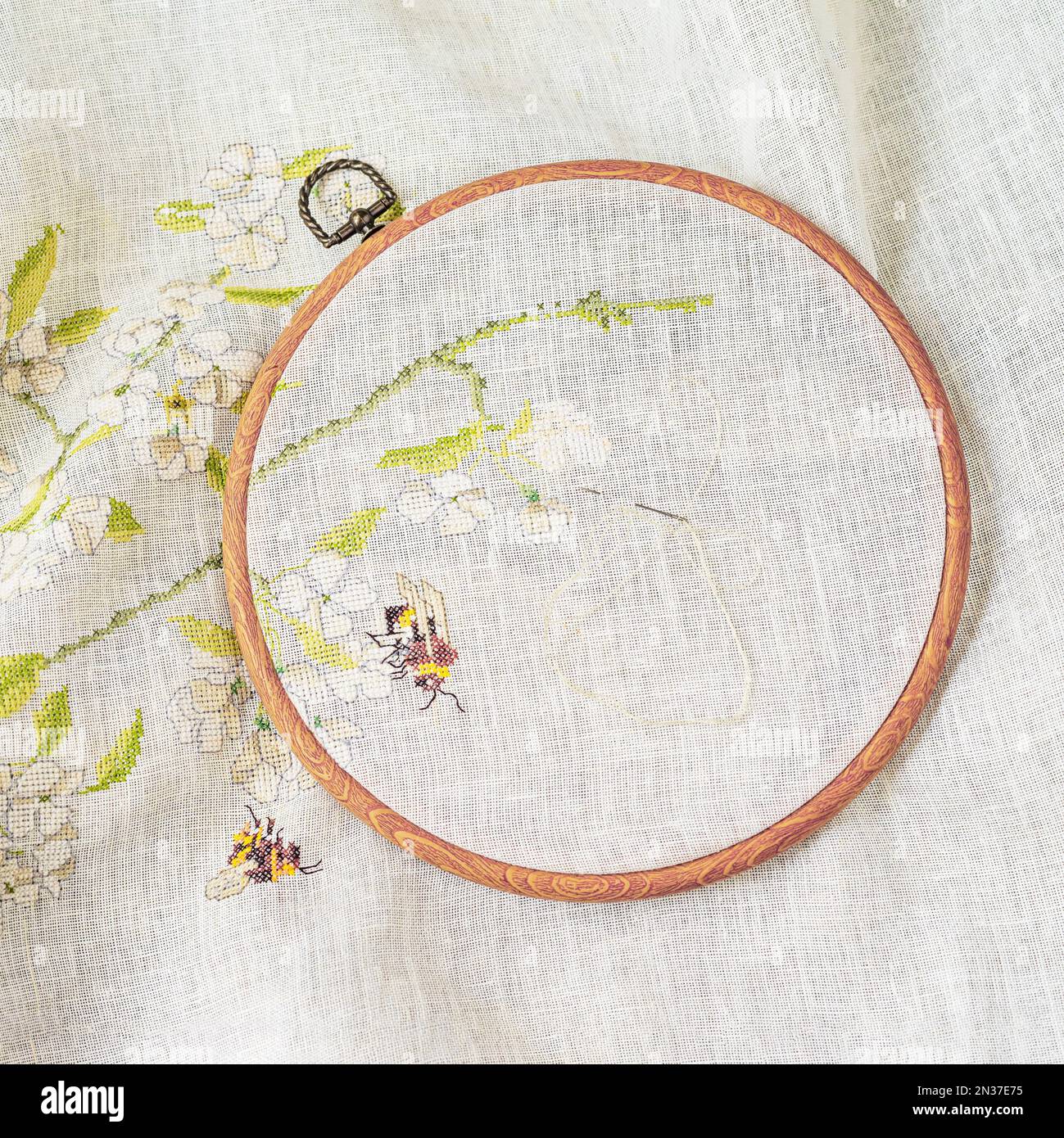 Hoops mit Holzstickerei, Draufsicht, Nadel mit Faden und Stoff mit Blumenmuster, Stickerei von Hand. Hobby und Handarbeit Stockfoto