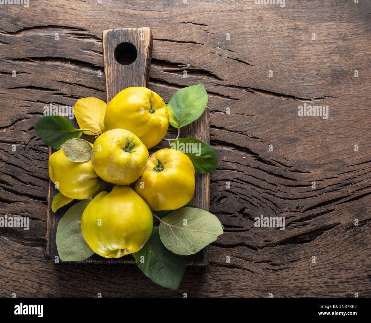 Reifer goldgelber Quittenfrucht-Holzhintergrund. Kleine Gruppe von Früchten mit Blättern, Draufsicht. Stockfoto