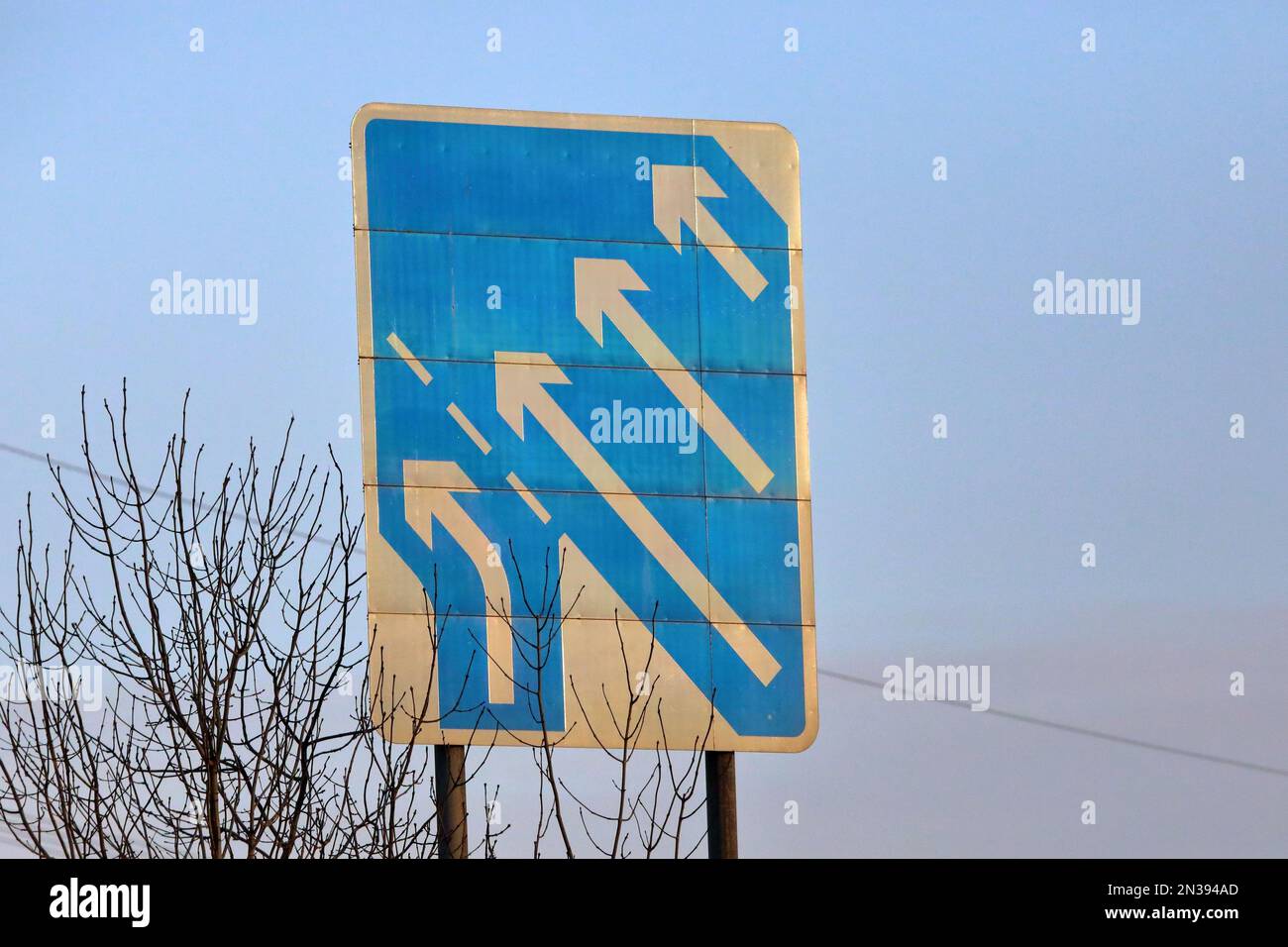 Autobahnschild, das darauf hinweist, dass die Zufahrtsstraße als Spurversatz auf die Hauptstraße trifft, um die Anzahl der Fahrspuren von drei auf vier zu erhöhen Stockfoto