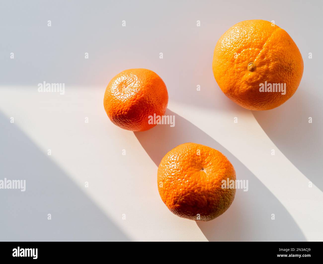 Drei Mandarinen auf weißem Hintergrund. Reife Früchte bei Sonnenlicht. Draufsicht auf leuchtend orangefarbene Zitronen mit diagonalen Schatten. Stockfoto