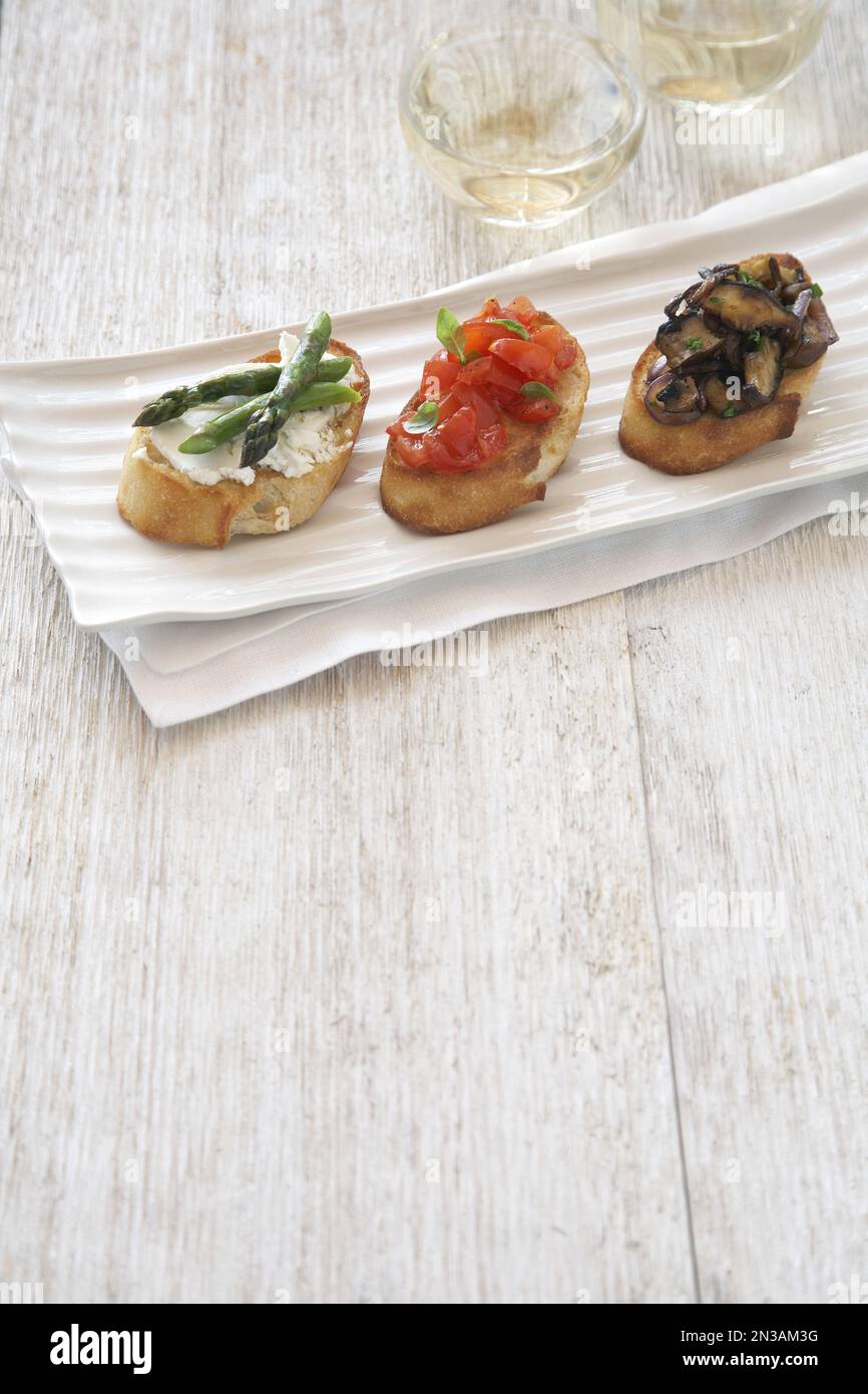 Crostini garniert mit Spargel, Tomaten und Pilzen, serviert auf einer Platte Stockfoto