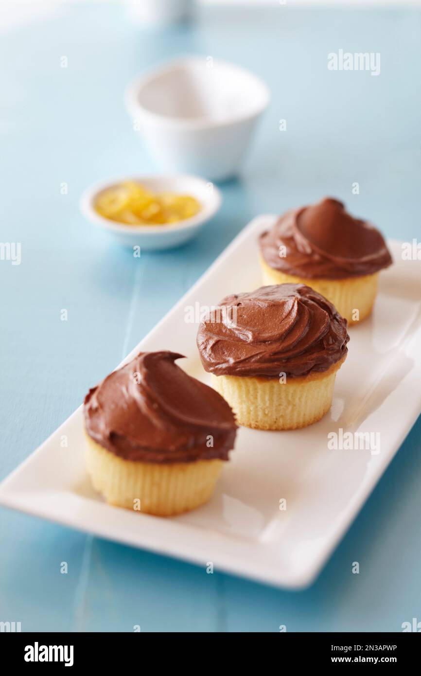 Schokoladen-Muffins auf blauem Hintergrund mit einer kleinen Schüssel Zitronenschale im Hintergrund Stockfoto