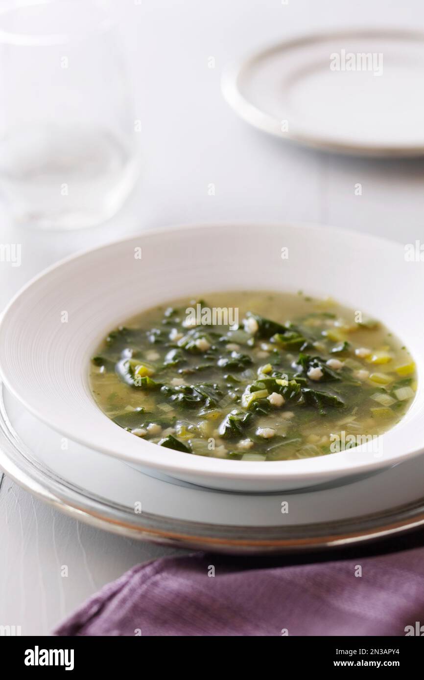 Schüssel mit grüner Blattsuppe mit sternförmiger Pasta auf weißem Hintergrund und einer violetten Serviette Stockfoto