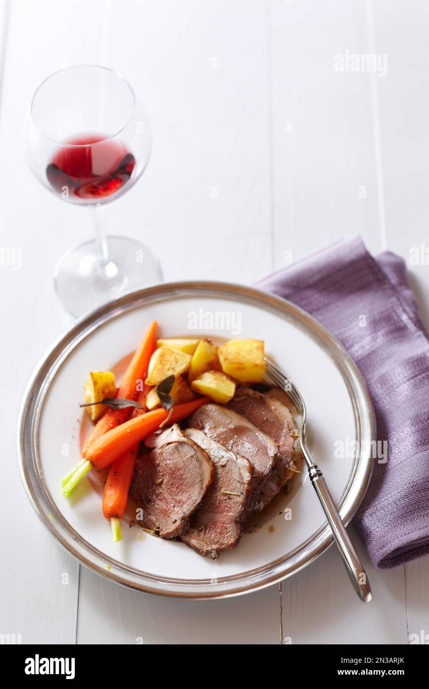 Lammteller mit Karotten, Kartoffeln und einem Glas Rotwein mit einer lila Serviette Stockfoto