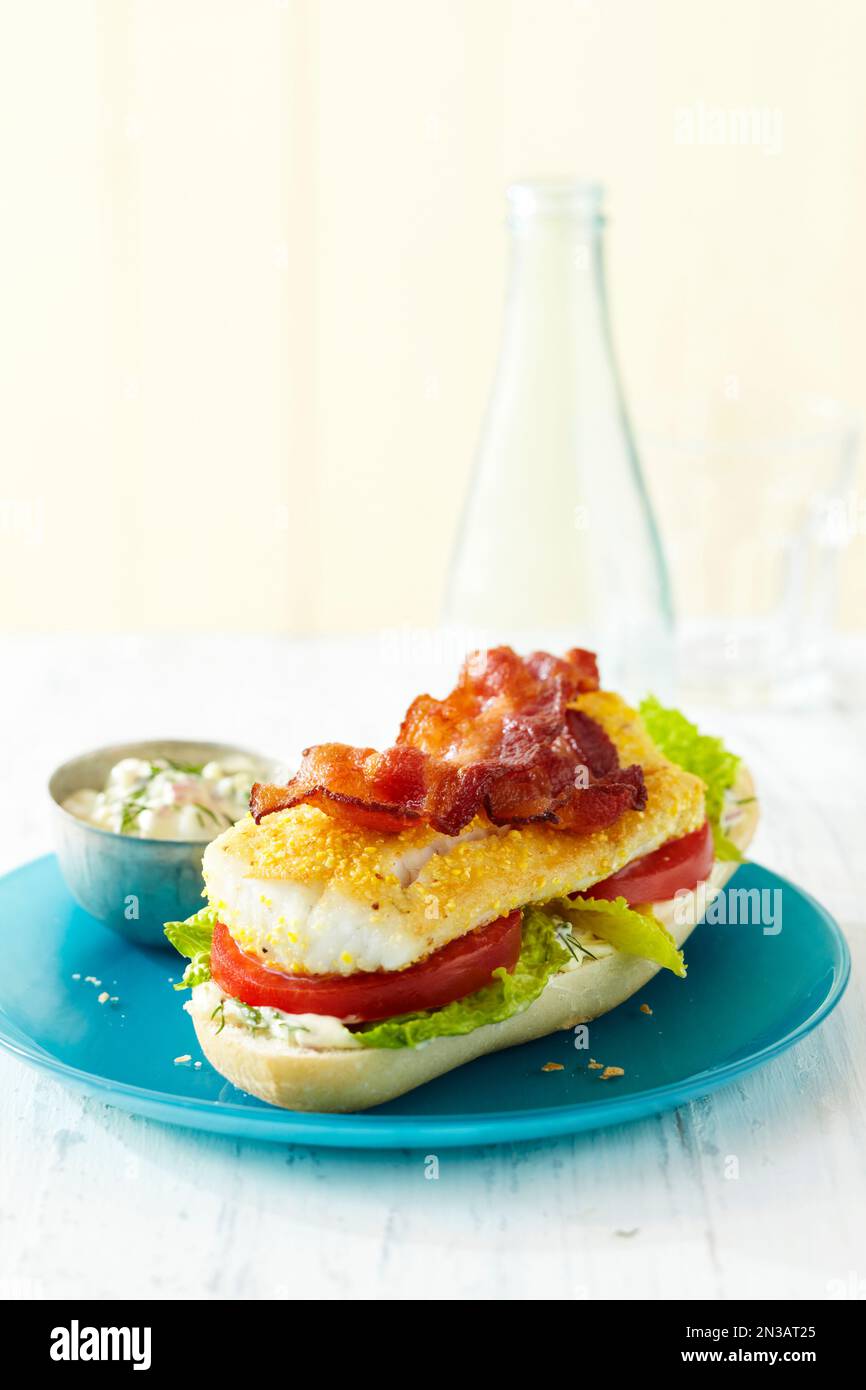 Offenes Sandwich mit Fisch mit Speck, Salat, Tomaten und Mayonnaise auf einem blauen Teller Stockfoto