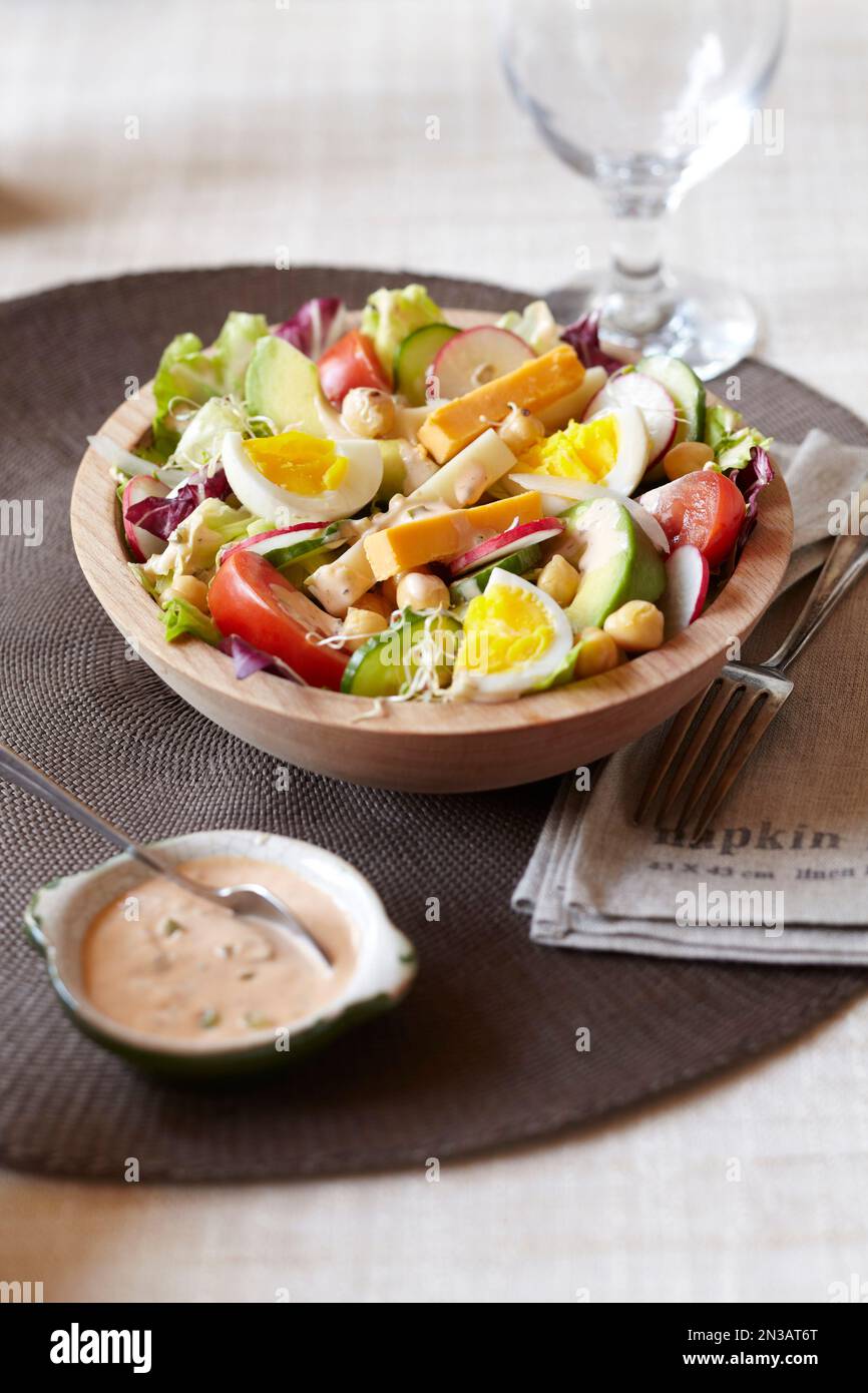 Salat garniert mit Eiern, Kichererbsen, Avocado, Rettich, Käse mit einem cremigen Dressing an der Seite Stockfoto