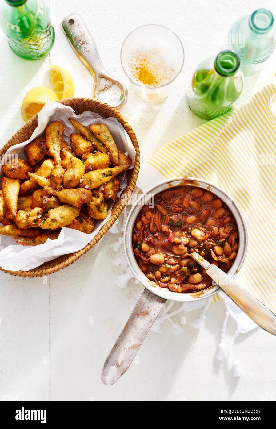 Gebackene Bohnen in einem Kochtopf mit frittiertem Okra in einem Korb und Flaschen Bier Stockfoto