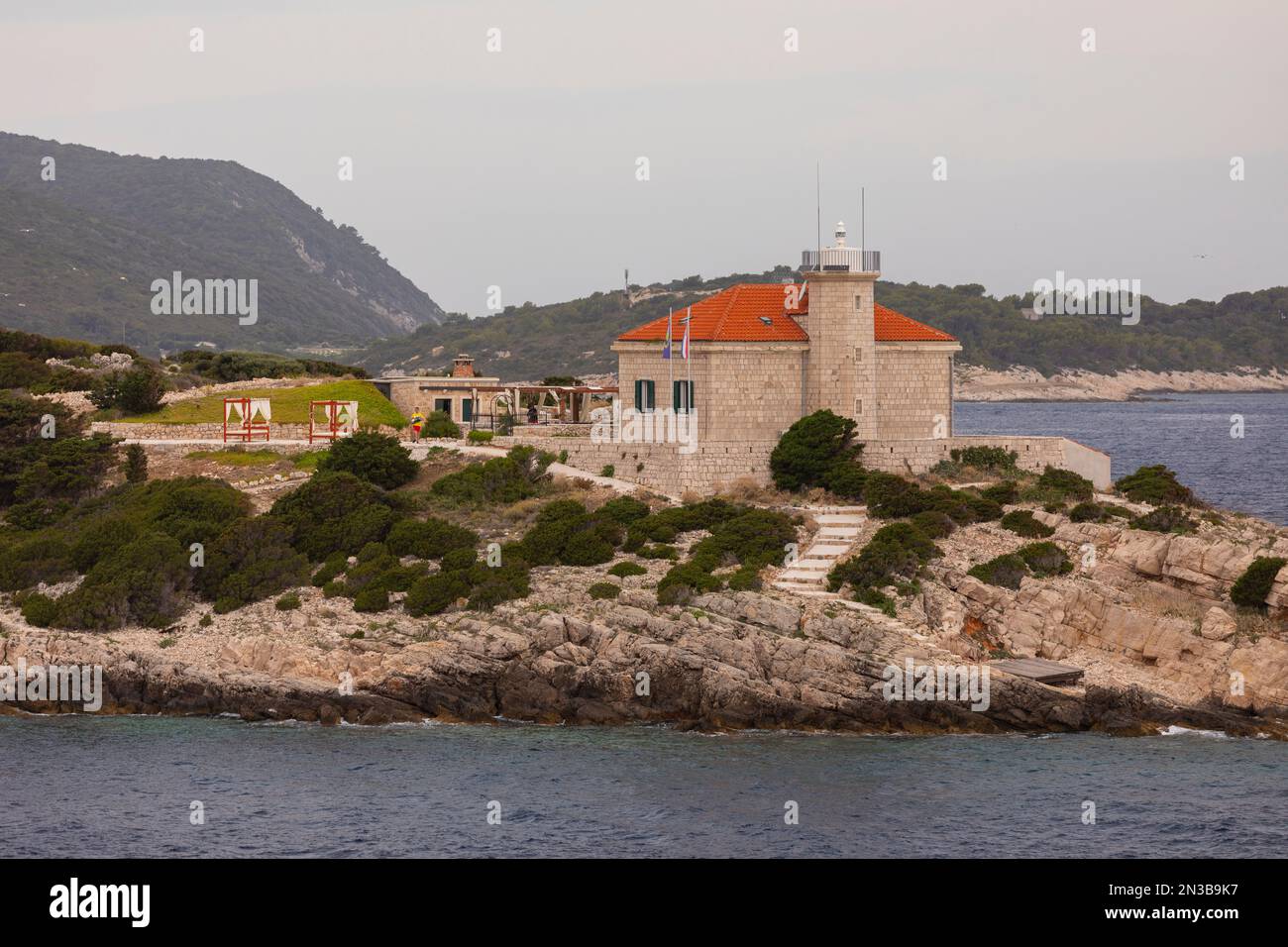 OTOCIC-GASTGEBER, VIS, KROATIEN, EUROPA - Leuchtturm auf der Host-Insel in der Nähe des Hafens von Vis, wie von Fort George aus gesehen, und Leuchtturm-Gebäude. Stockfoto