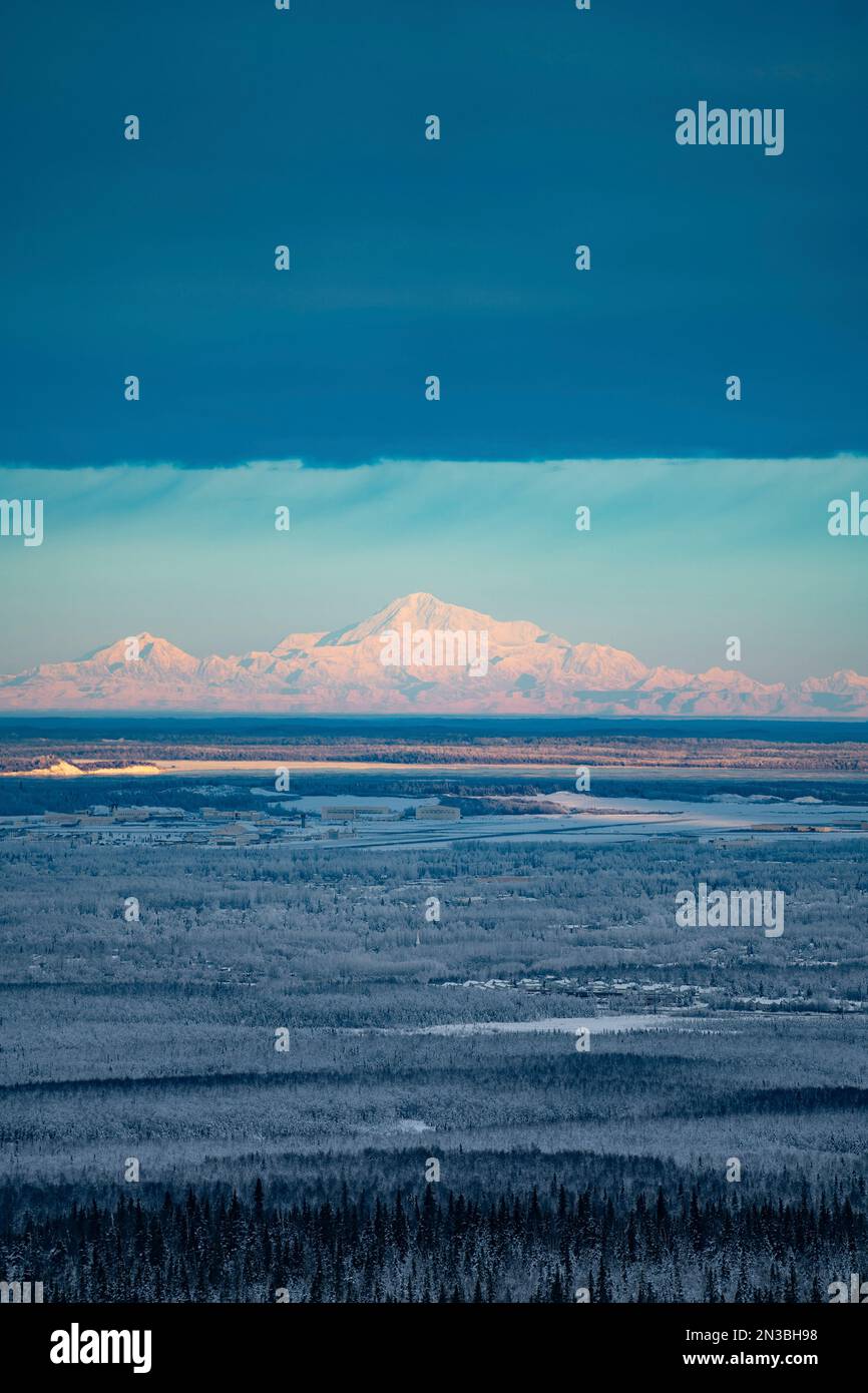 Der Berg Denali scheint in der Sonne unter den Wolken über den frostigen Winterbäumen und Anchorage Alaska mit der Joint Base Elmendorf Richardson Military... Stockfoto