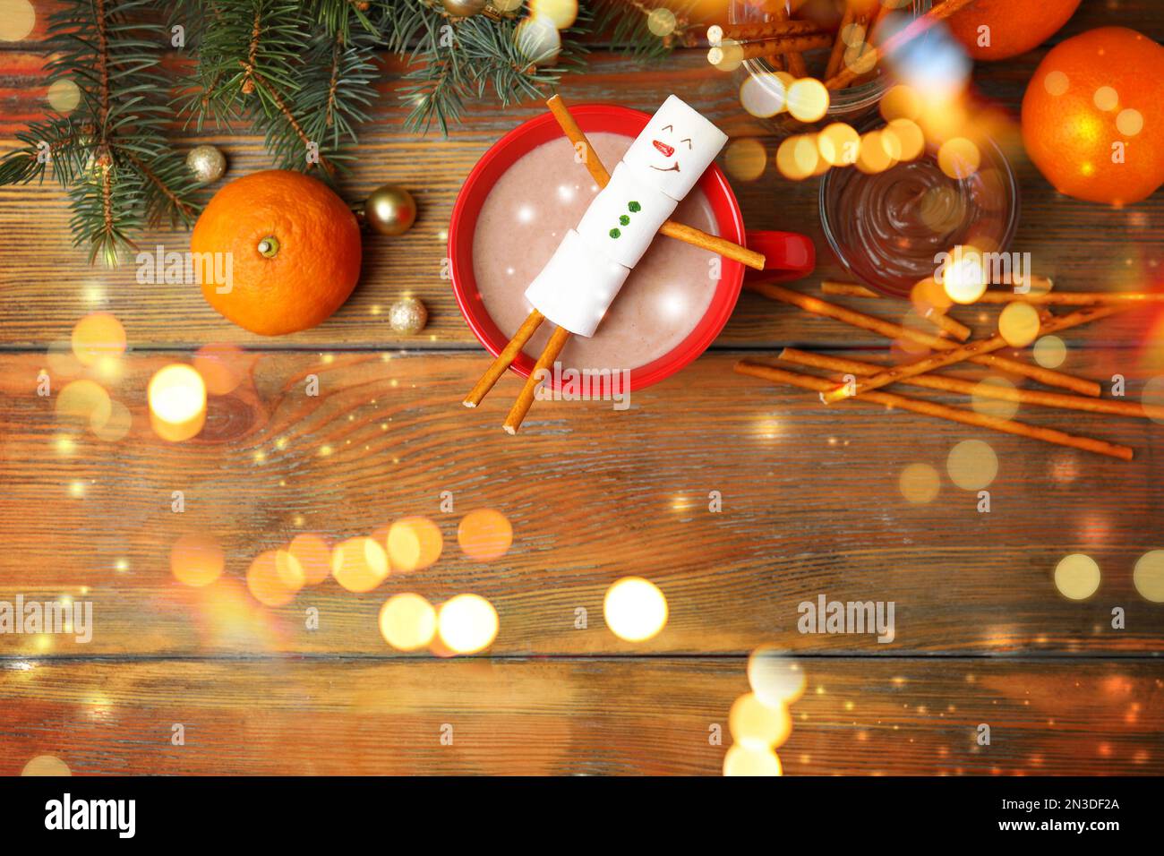 Flache Liegezusammensetzung mit Marshmallow-Schneemann in einer Tasse heißes Getränk auf einem Holztisch, Platz für Text. Bokeh-Effekt Stockfoto