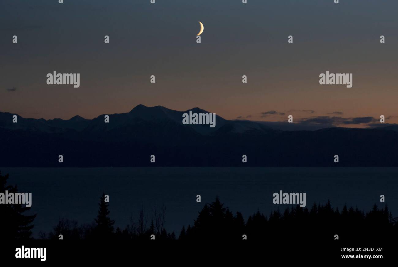 Silhouette der Kenai Mountains mit Mondaufgang über der Kachemak Bay in der Abenddämmerung; Homer, Alaska, Vereinigte Staaten von Amerika Stockfoto