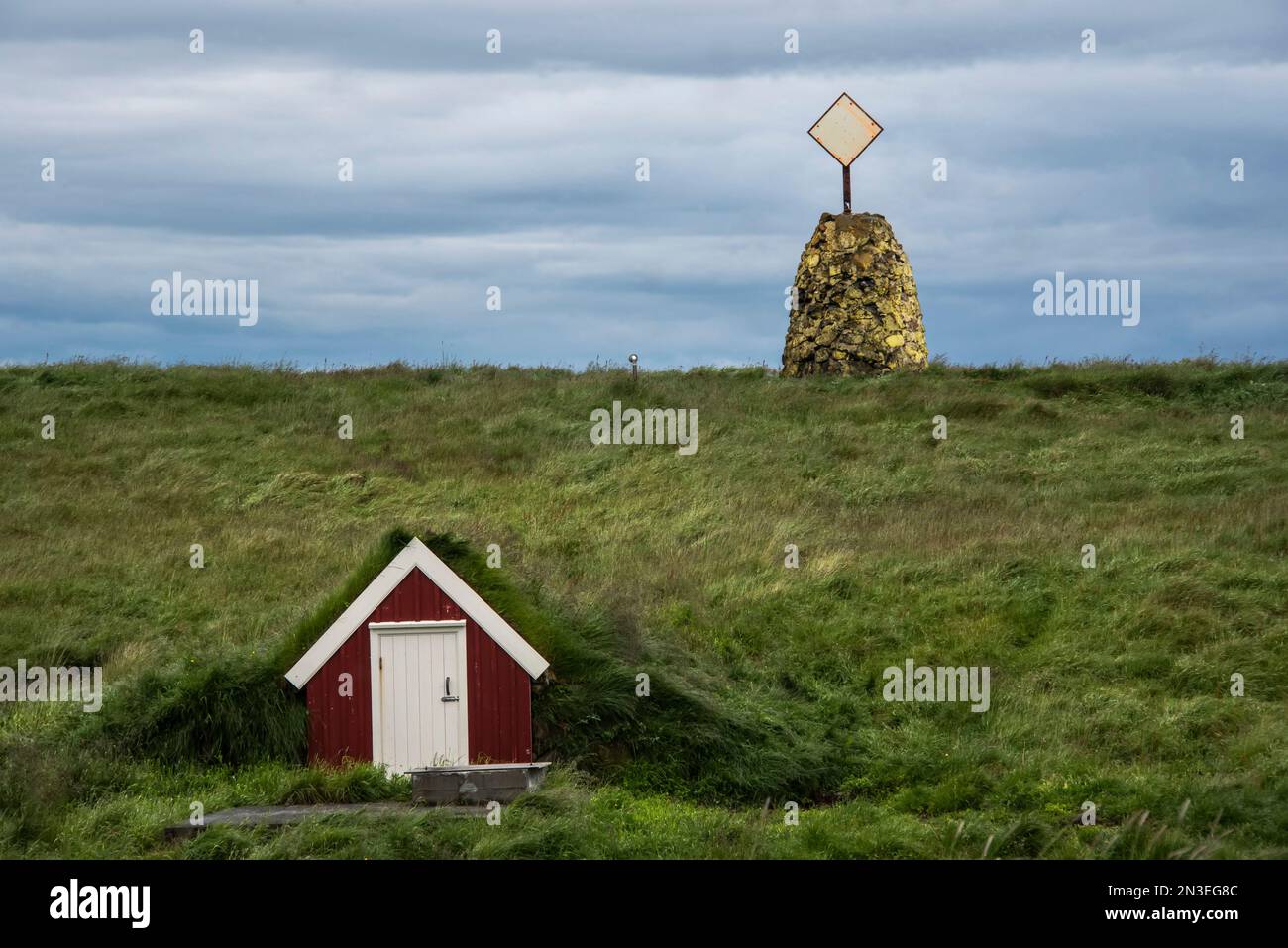 Lagerungsstruktur an der Seite eines Grashügels und Steinformation mit Radarreflektor auf dem Hügel auf Flatey Island, einem ehemaligen Fischerdorf o... Stockfoto