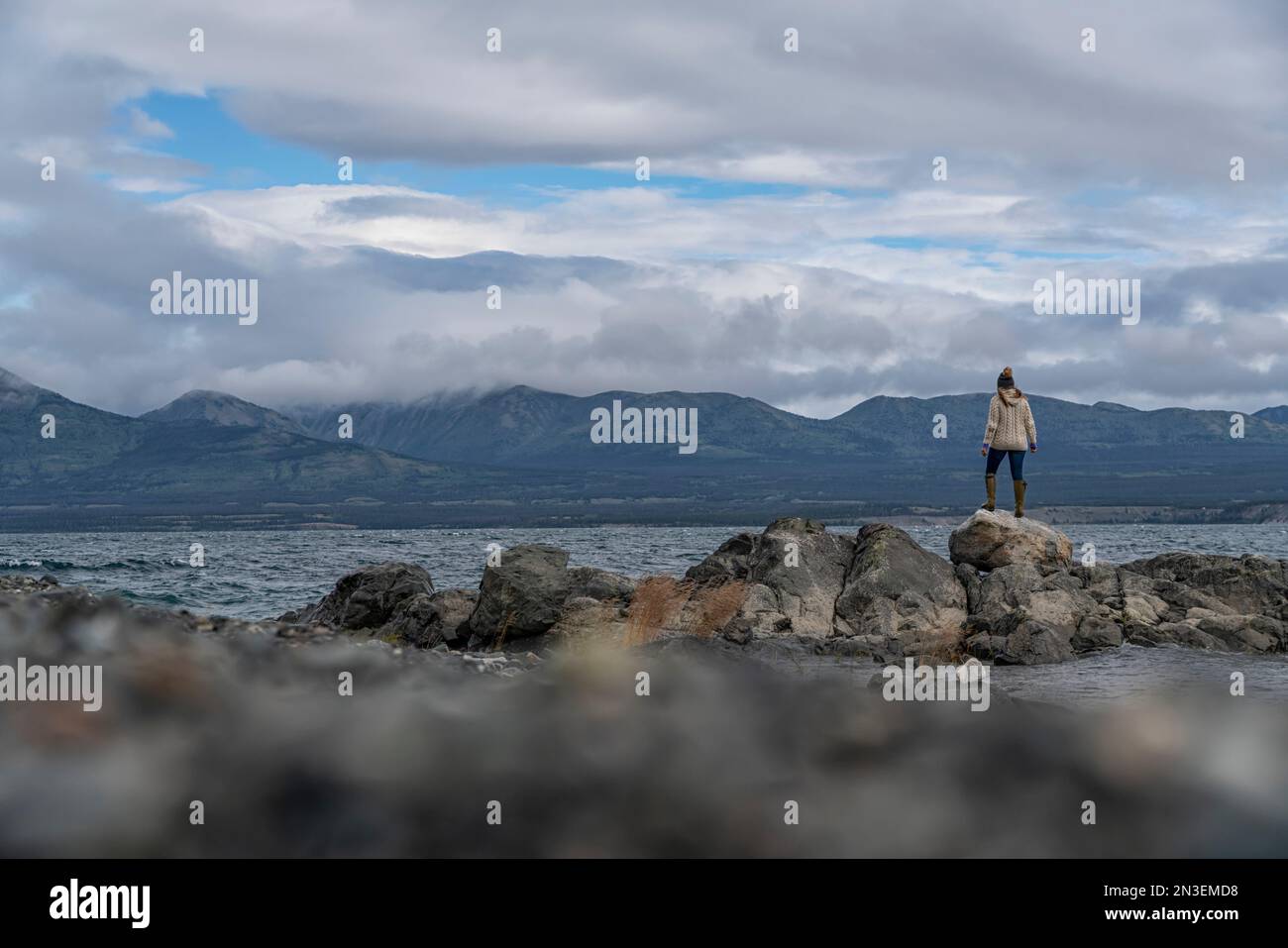 Blick von hinten auf eine Frau, die am felsigen Ufer des Kluane Lake steht; Yukon, Kanada Stockfoto