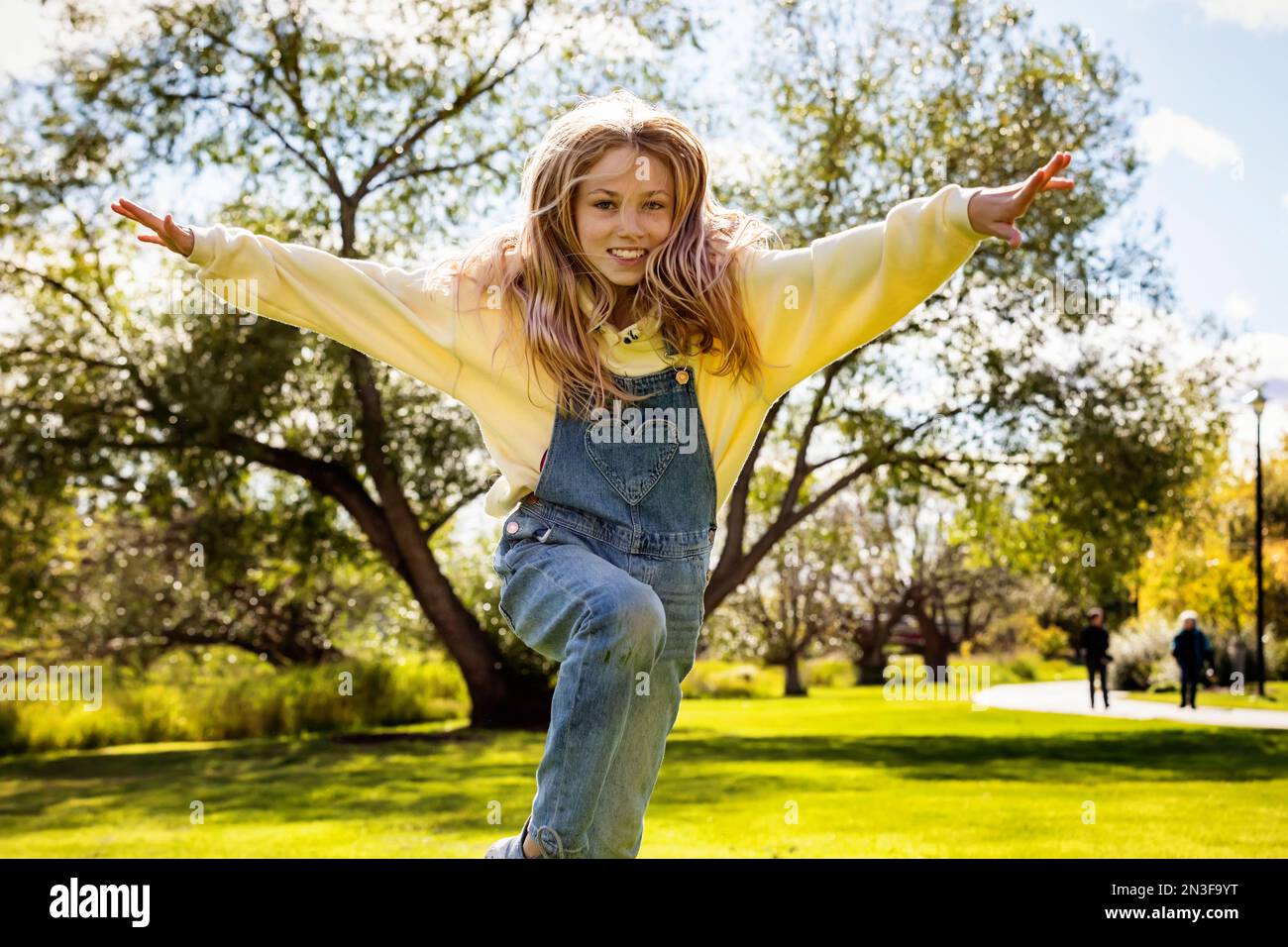 Ein junges Mädchen mit langen blonden Haaren läuft über das Gras und springt an einem warmen Herbsttag in einem Stadtpark auf die Kamera zu Stockfoto