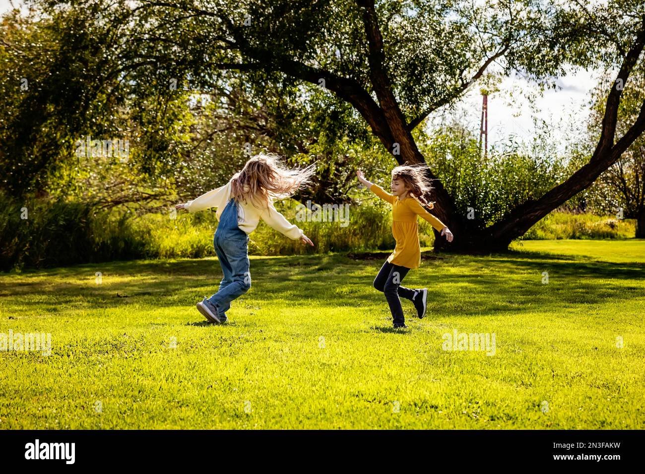 Zwei Schwestern genießen die Gesellschaft des anderen und spielen und drehen gemeinsam an einem warmen Herbsttag in einem Stadtpark; St.. Albert, Alberta, Kanada Stockfoto