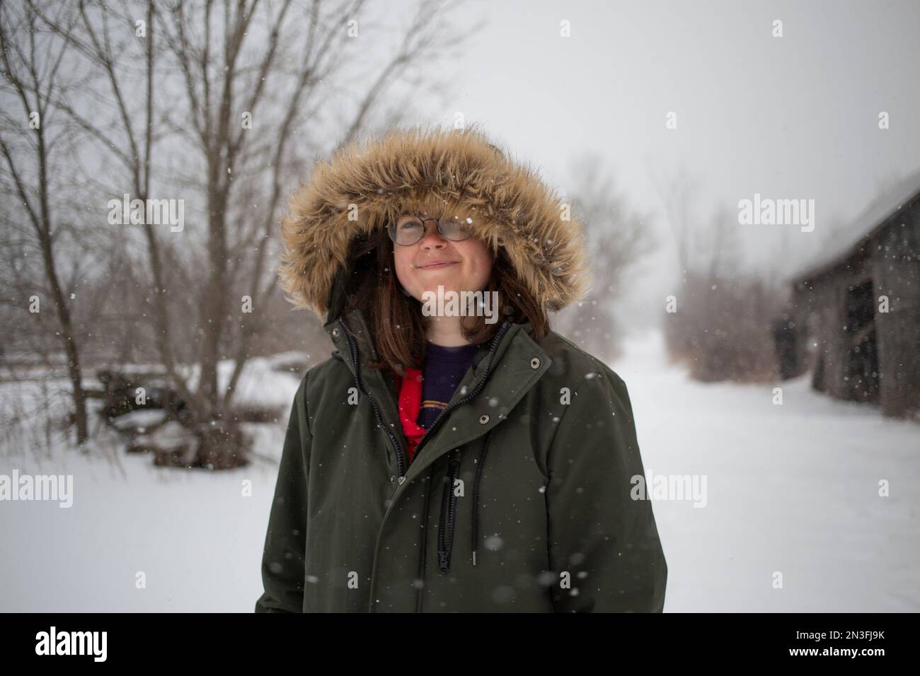 Eine Frau in einer Tannenbesatz-Kapuzenjacke steht draußen und genießt einen Schneefall an einem Wintertag; Ottawa Valley, Ontario, Kanada Stockfoto