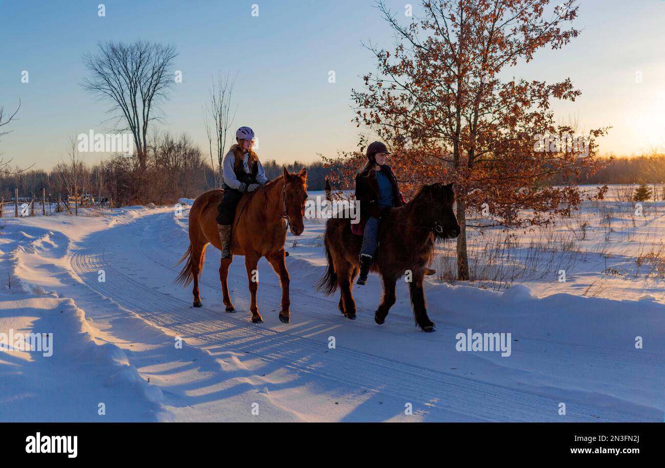 Mutter und Tochter reiten im Winter gemeinsam auf einer freigelegten Landstraße; Ottawa Valley, Ontario, Kanada Stockfoto
