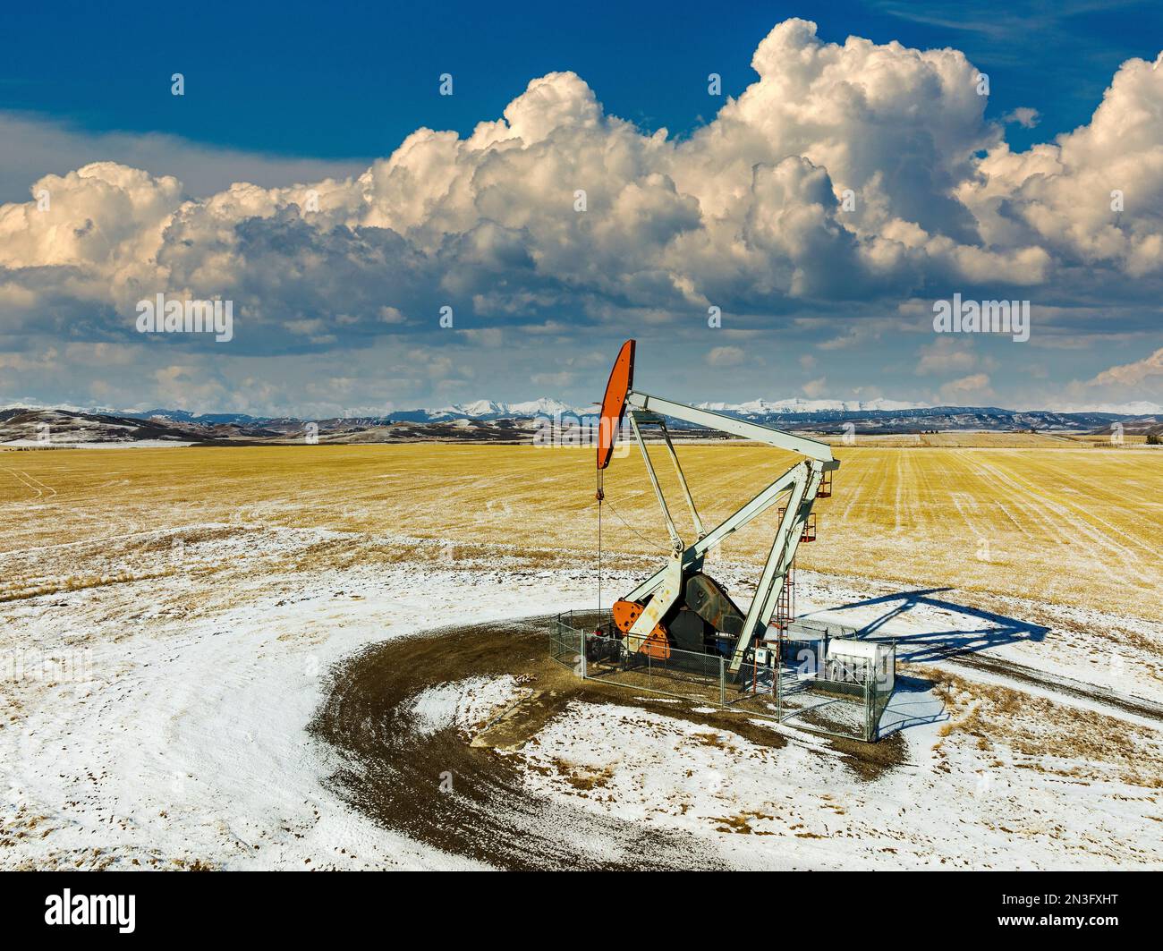 Luftaufnahme eines Kürbiss in einem schneebedeckten Feld mit dramatischen Wolken, blauem Himmel und schneebedeckten Bergketten im Hintergrund Stockfoto