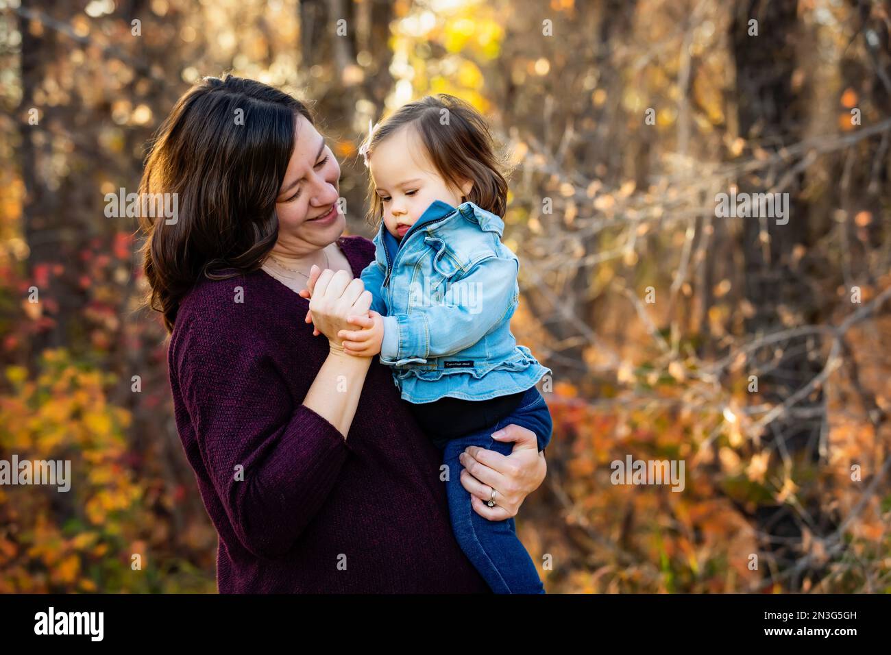 Porträt einer Mutter und ihres kleinen Mädchens mit Down-Syndrom, die während eines Familienausflugs in einem Stadtpark im Herbst eine schöne Zeit im Freien verbringen Stockfoto