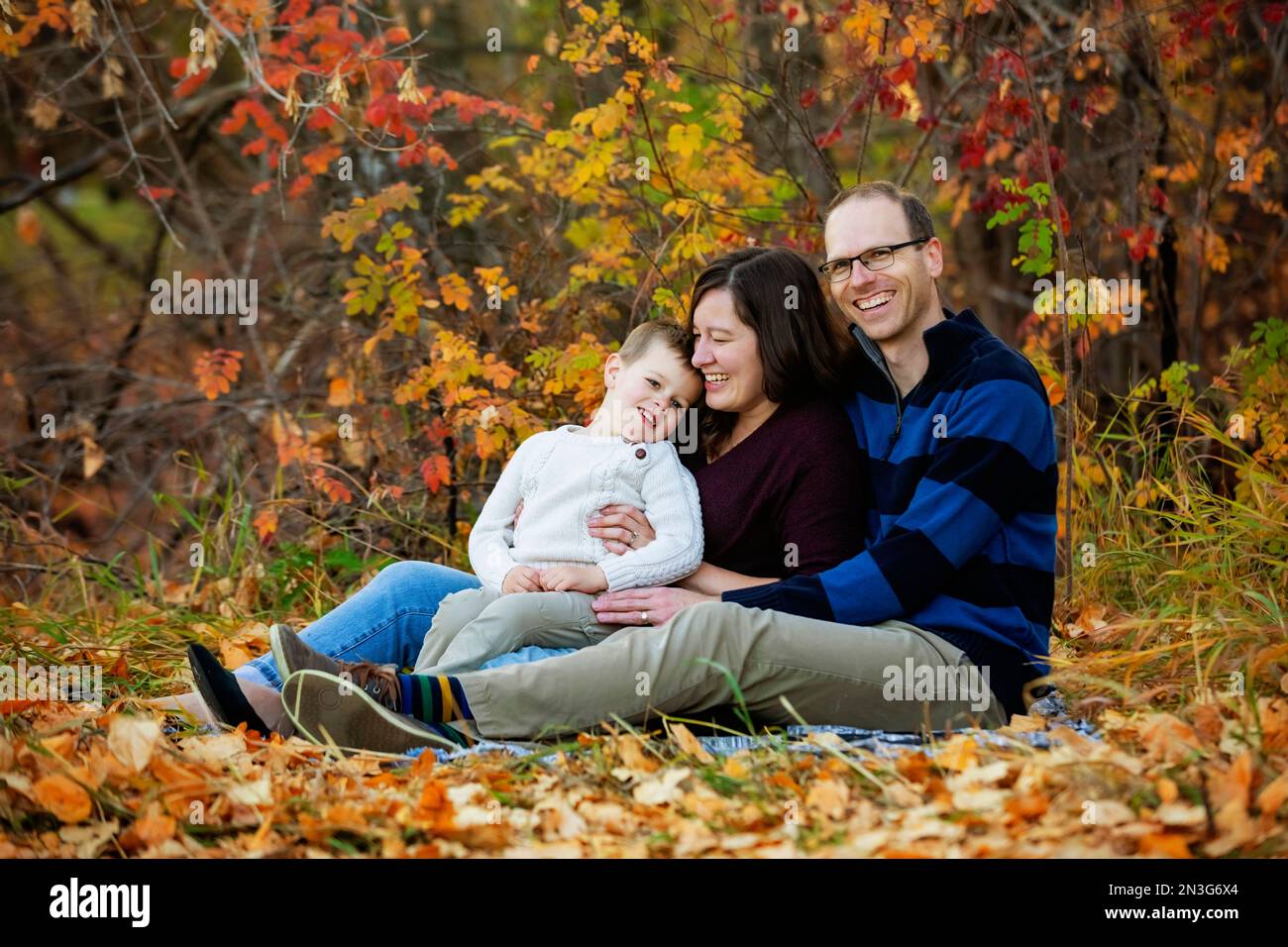 Eine Mutter und ein Vater verbringen während eines Familienausflugs in einem Stadtpark im Herbst zusammen mit ihrem Sohn etwas Zeit Stockfoto