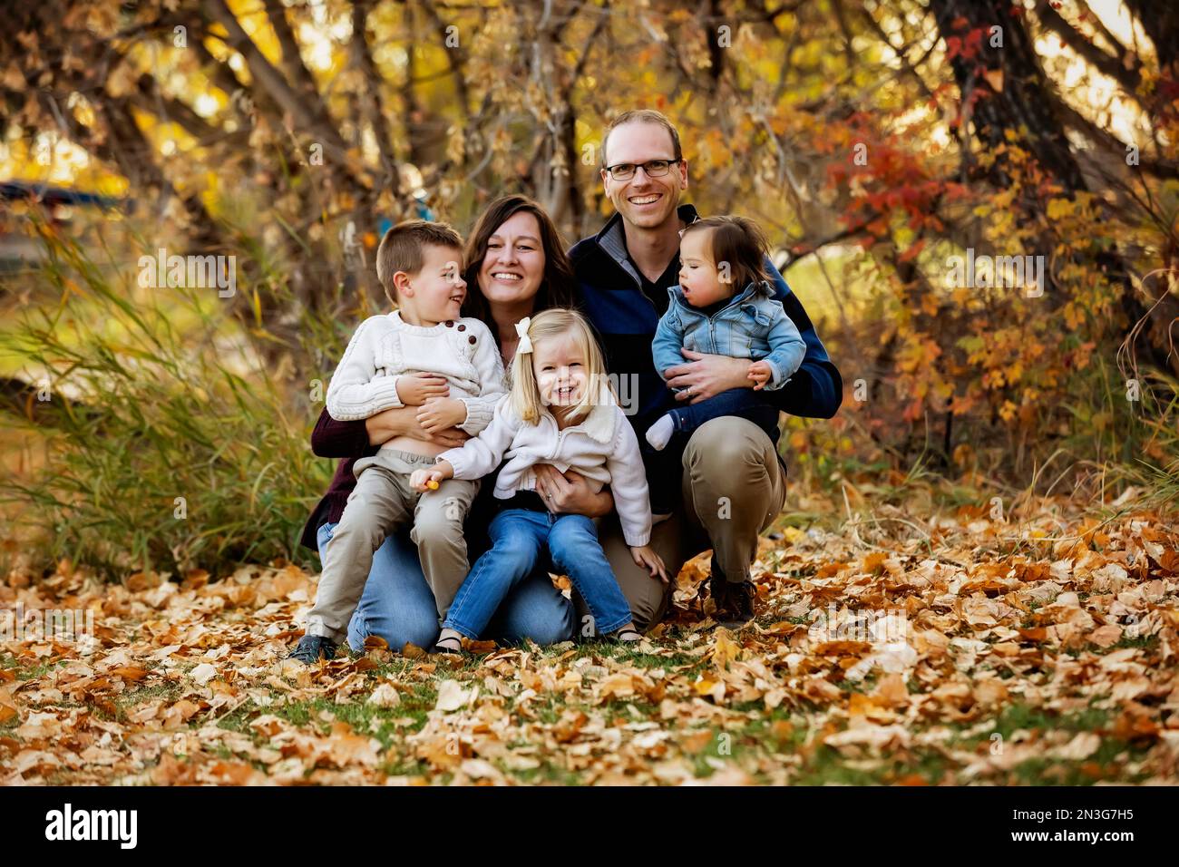 Porträt einer jungen Familie mit drei Kindern, jüngste Tochter mit Down-Syndrom, in einem Stadtpark während der Herbstsaison Stockfoto