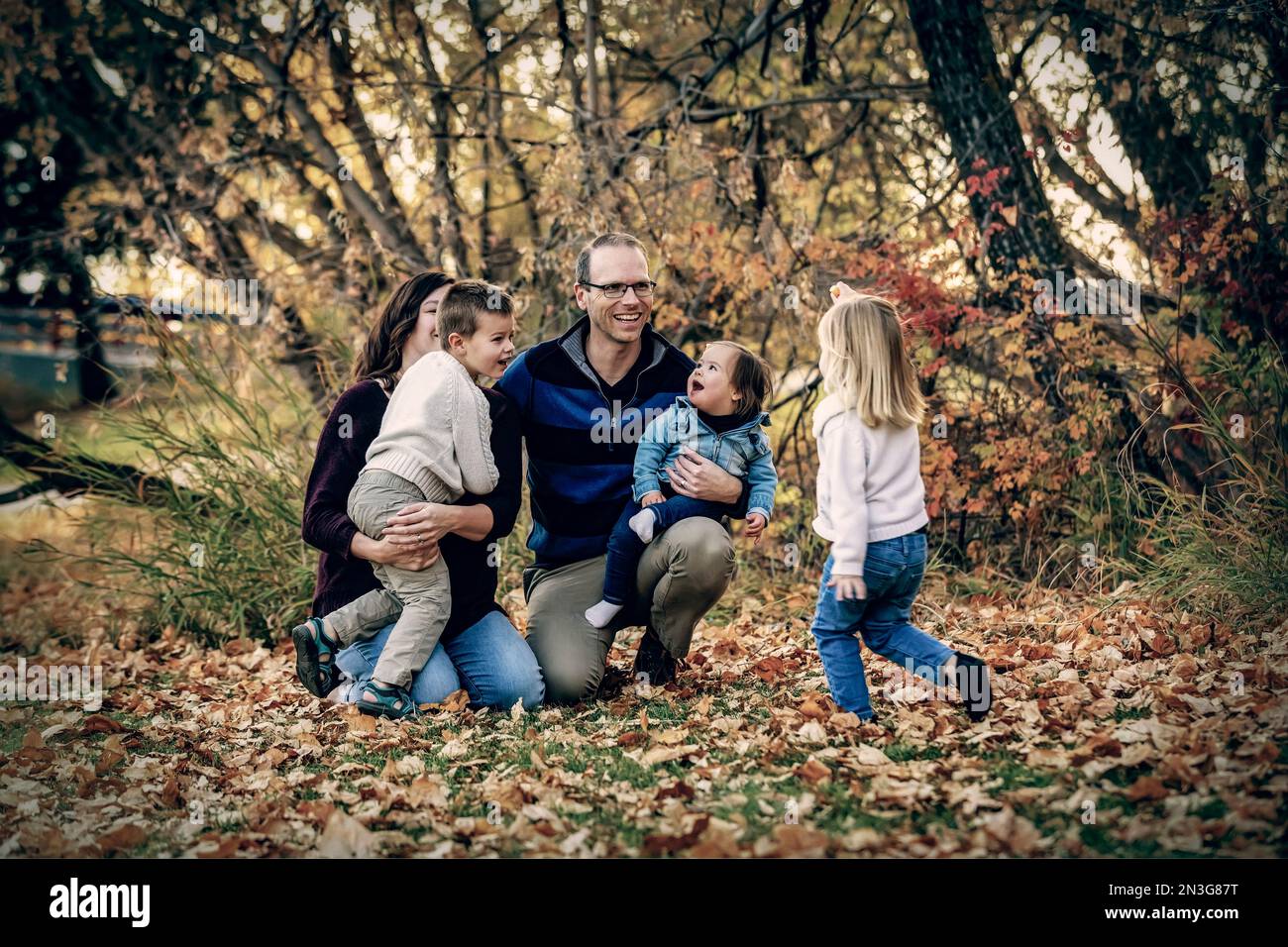 Junge Familie mit drei Kindern, jüngste Tochter mit Down-Syndrom, die in der Herbstsaison gemeinsam in einem Stadtpark Spaß hat Stockfoto